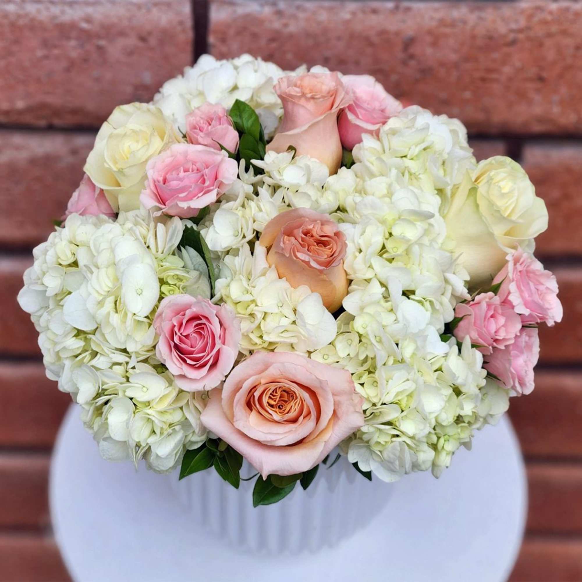 Pink and peach roses arranged with white hydrangeas in a white vase.