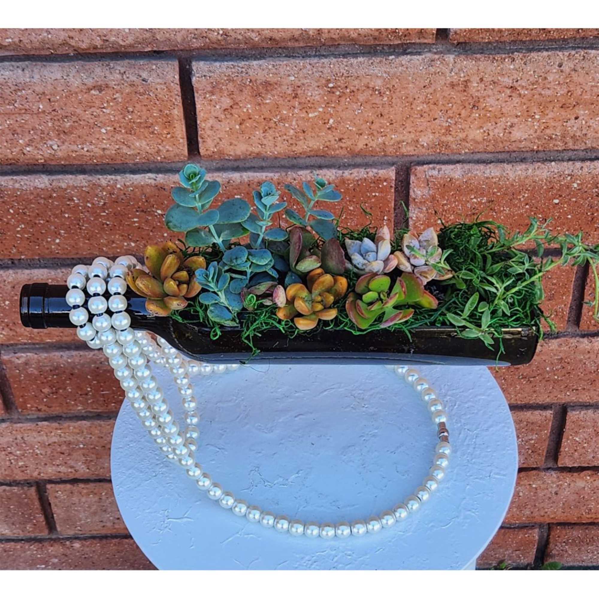 Succulent arrangement in a wine bottle with pearl strands draped over it