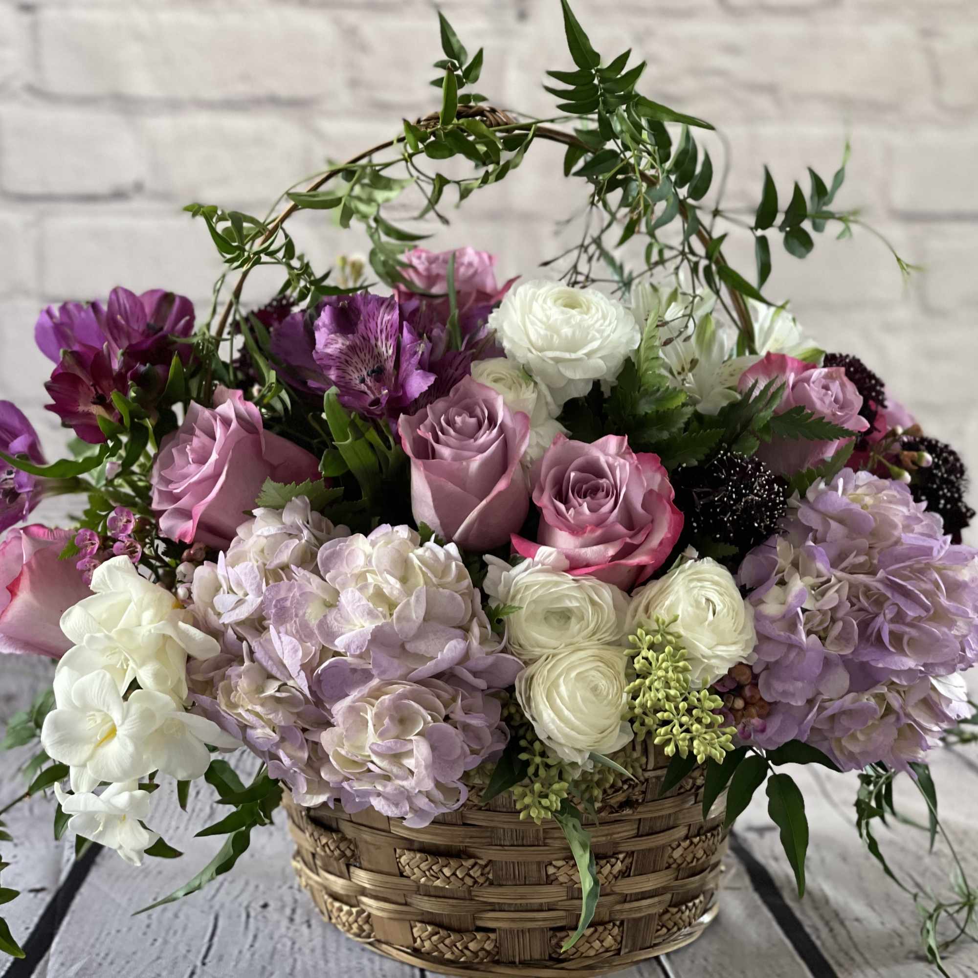 Basket arrangement of pink roses, hydrangeas, and white ranunculus