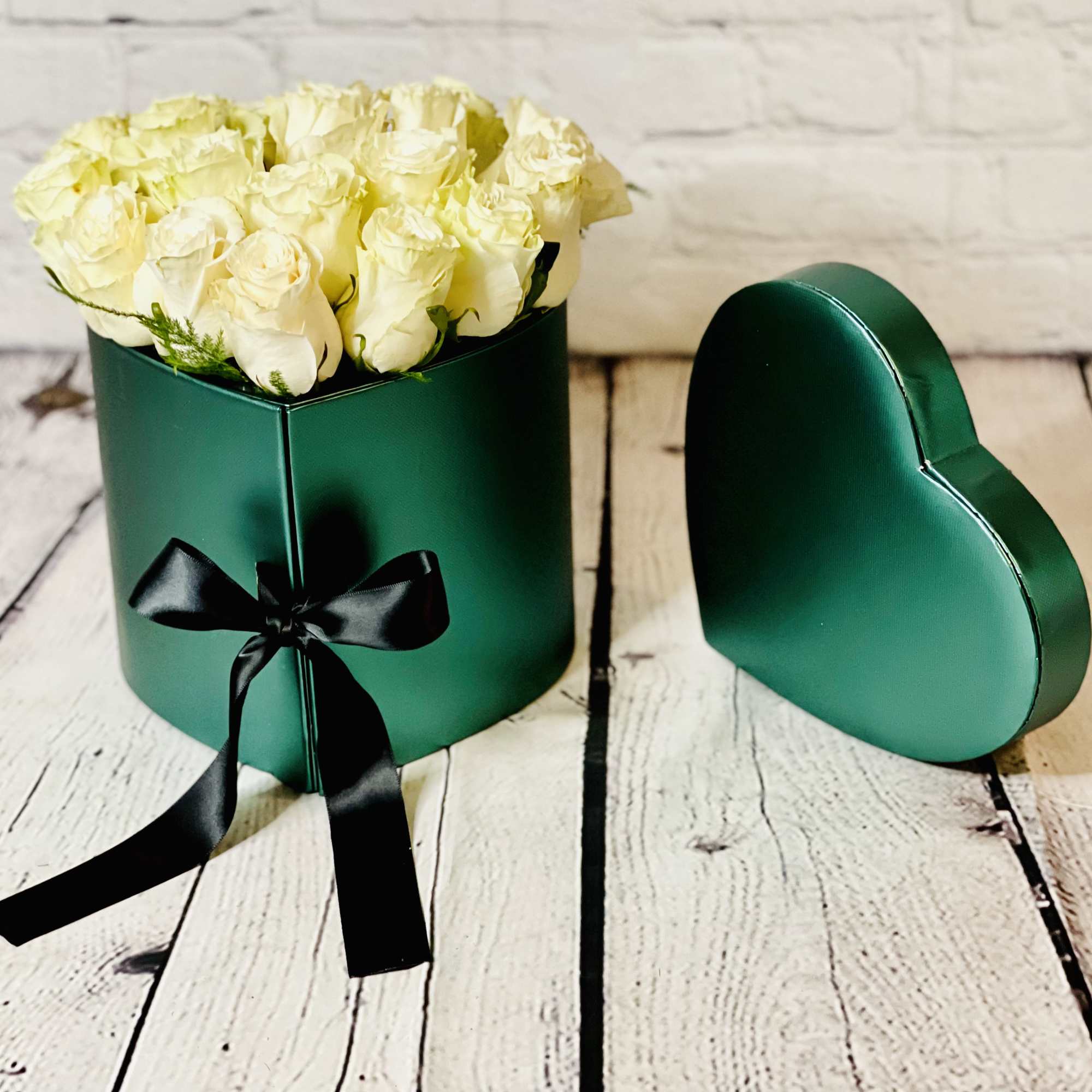 White roses in a green heart-shaped box with a black ribbon