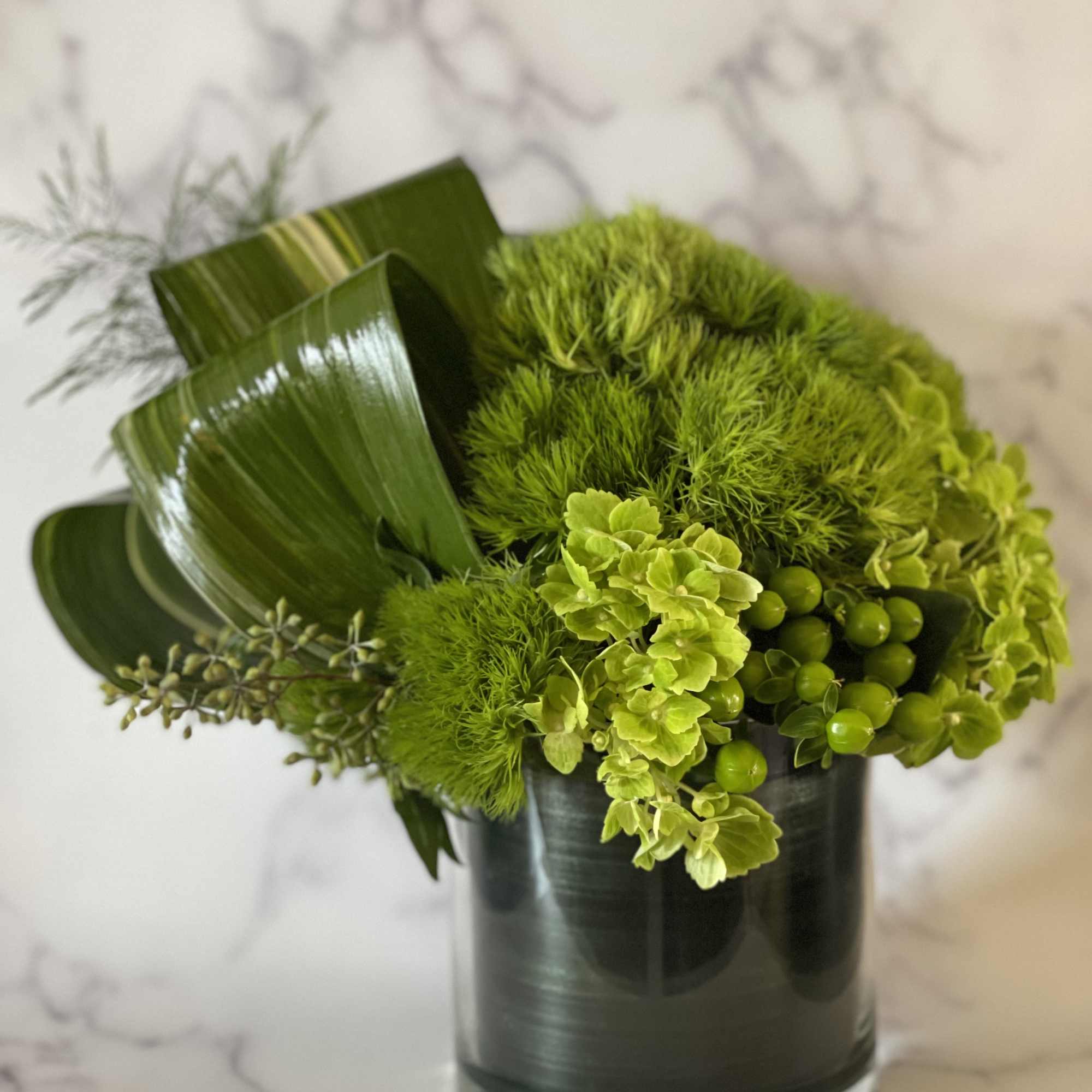 Green floral arrangement in a dark glass vase