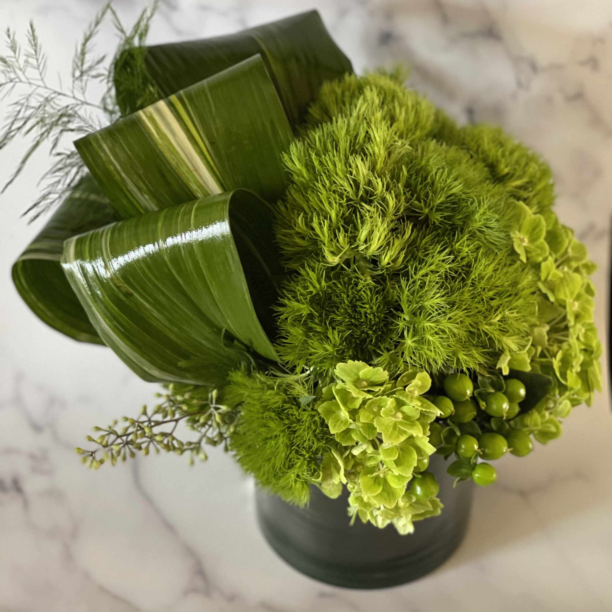Green floral arrangement in a dark vase with curled leaves and clustered blooms