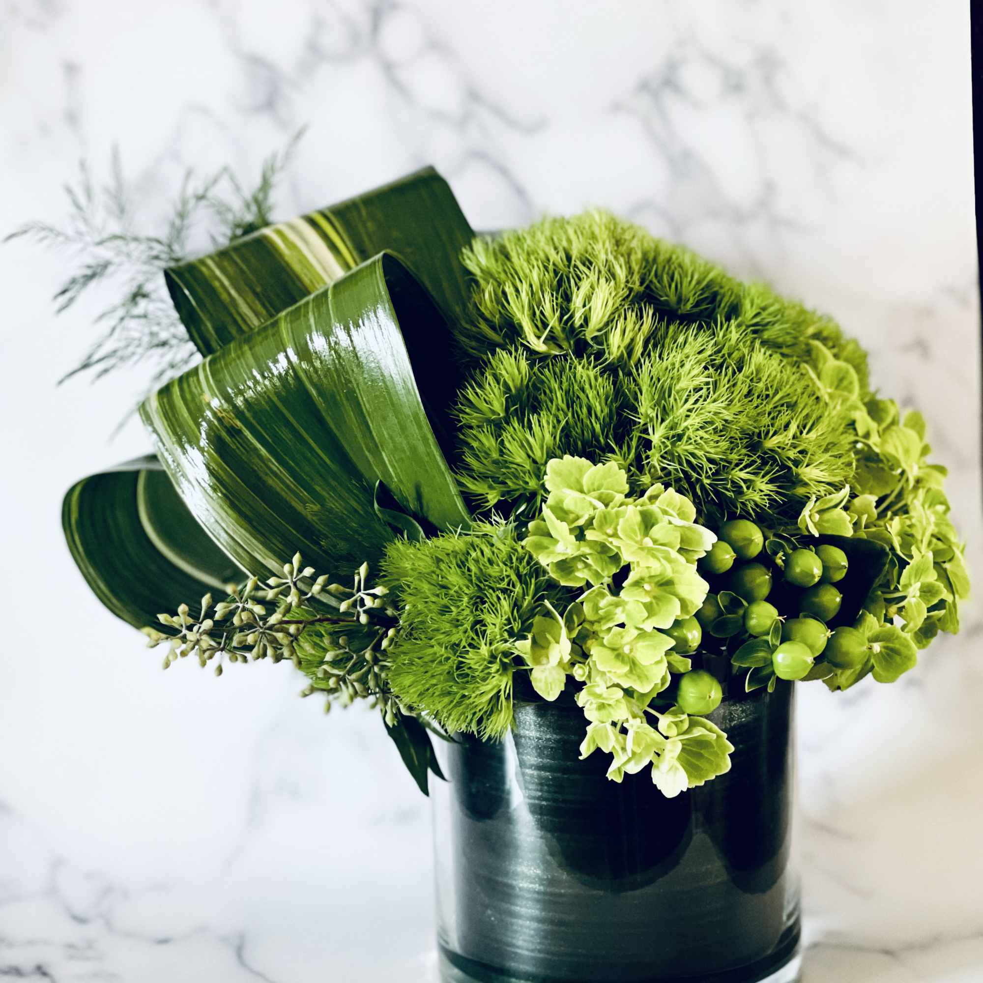Green floral arrangement in a dark glass vase with broad leaves