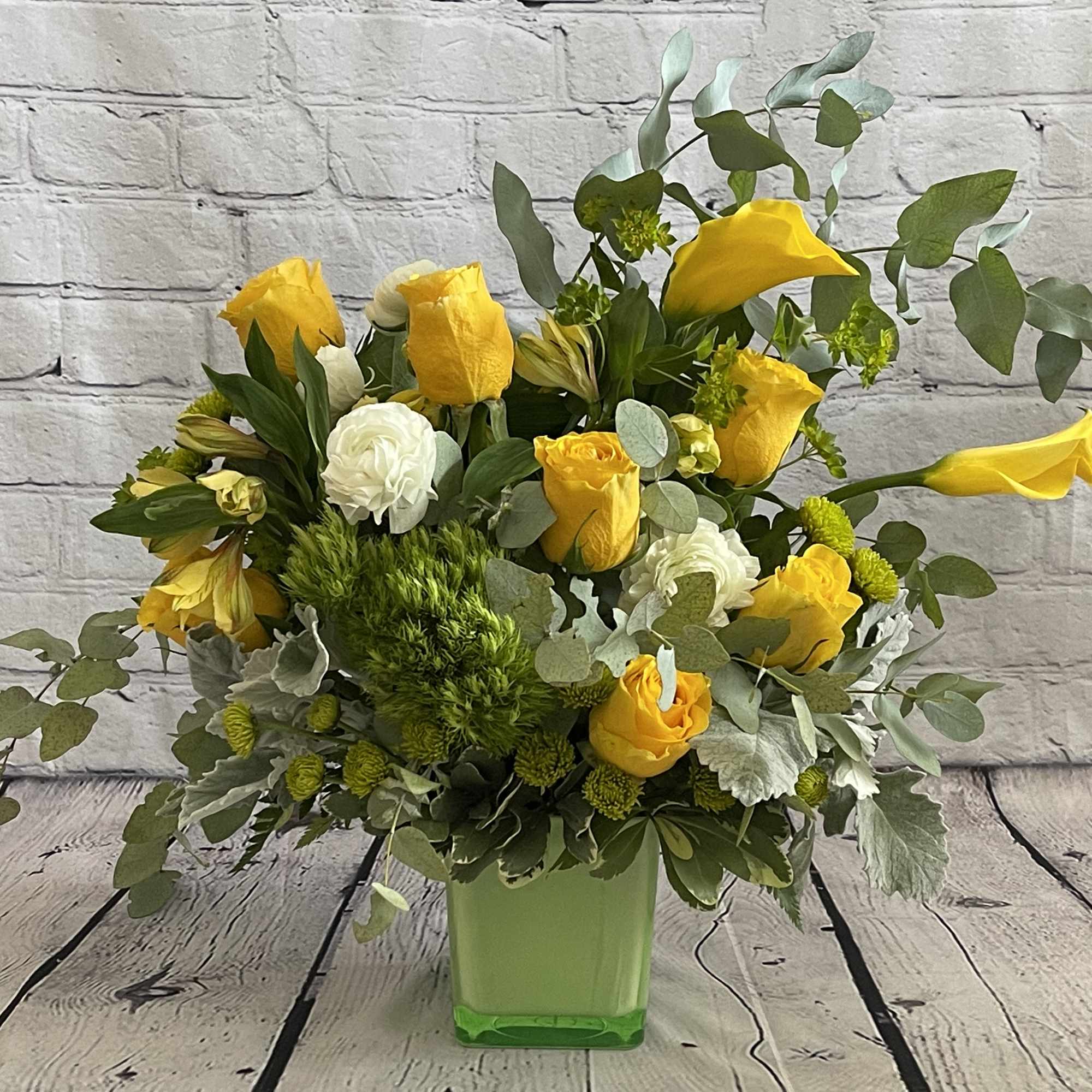 Yellow roses and white blooms in a green square vase
