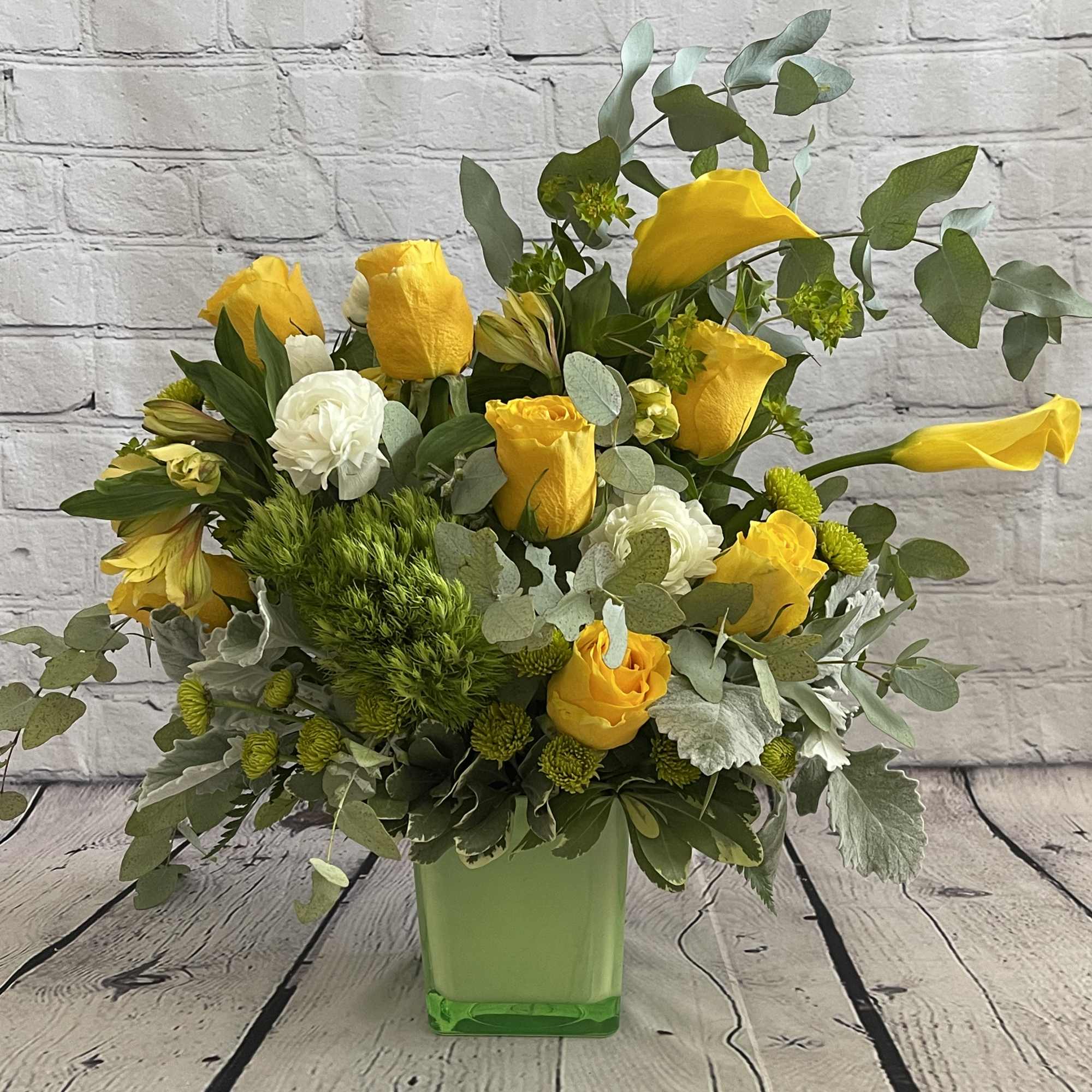 Yellow roses and white blooms arranged in a green square vase