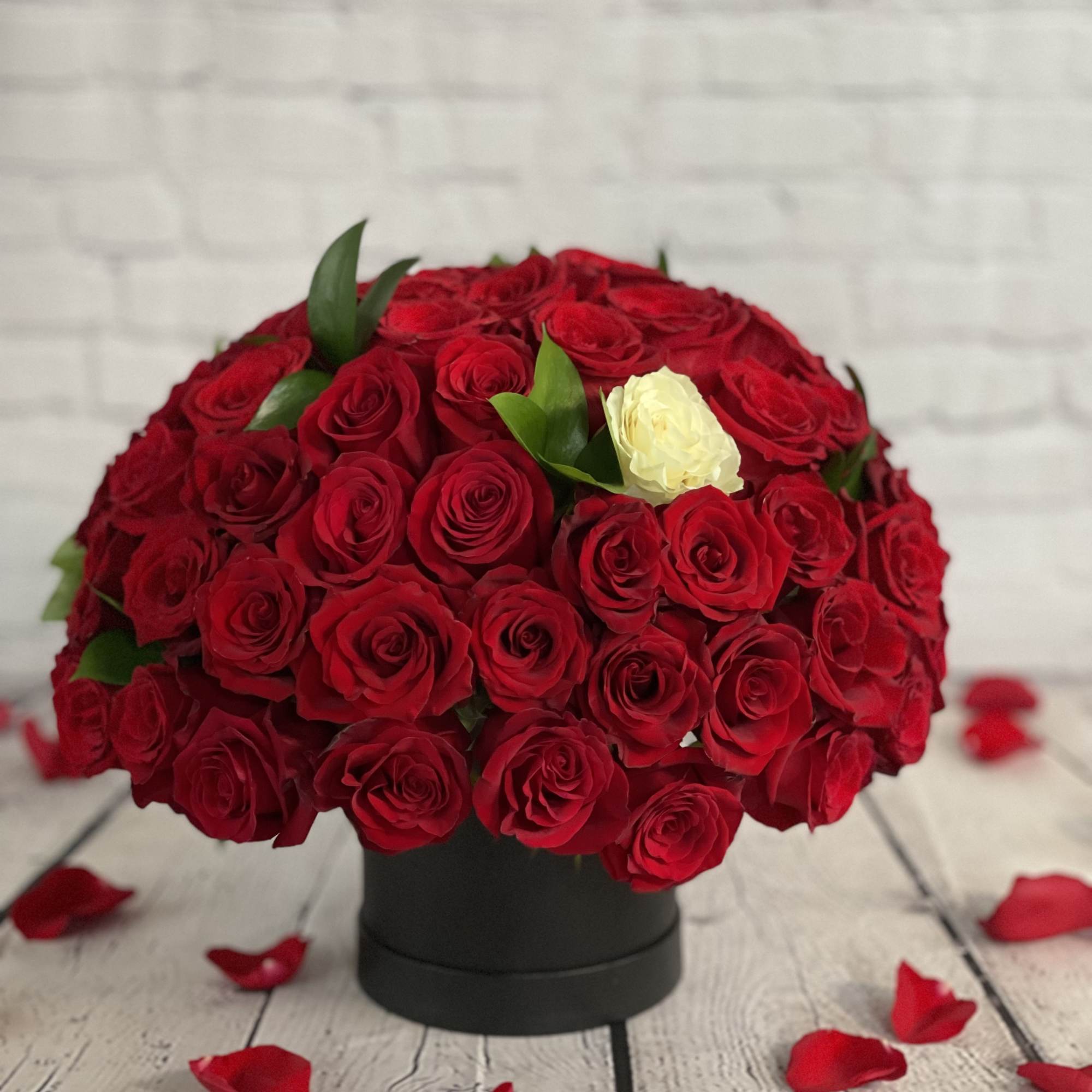 Round bouquet of red roses with one white rose in a black box