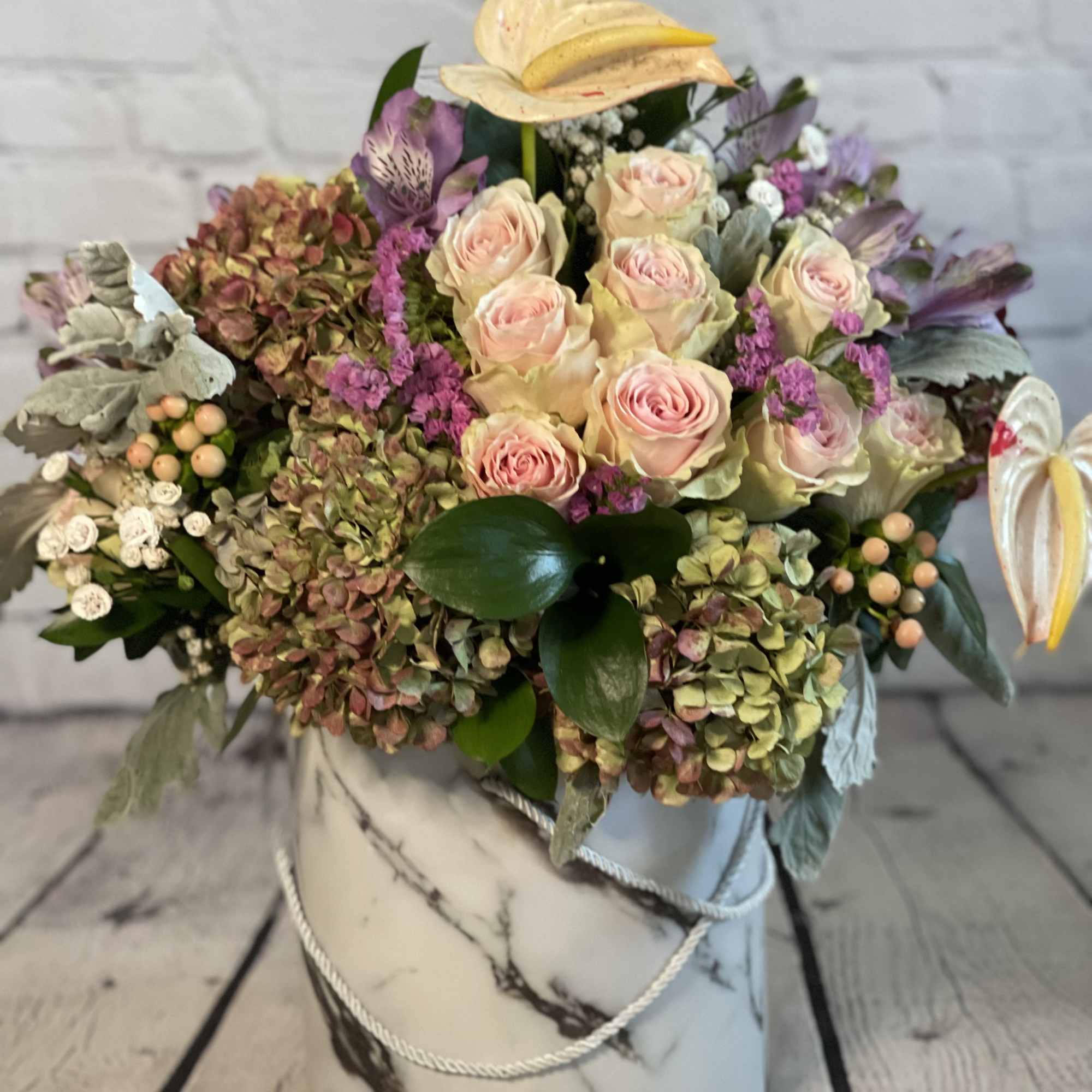 Mixed bouquet of pale pink roses and hydrangeas in a marble-patterned hat box