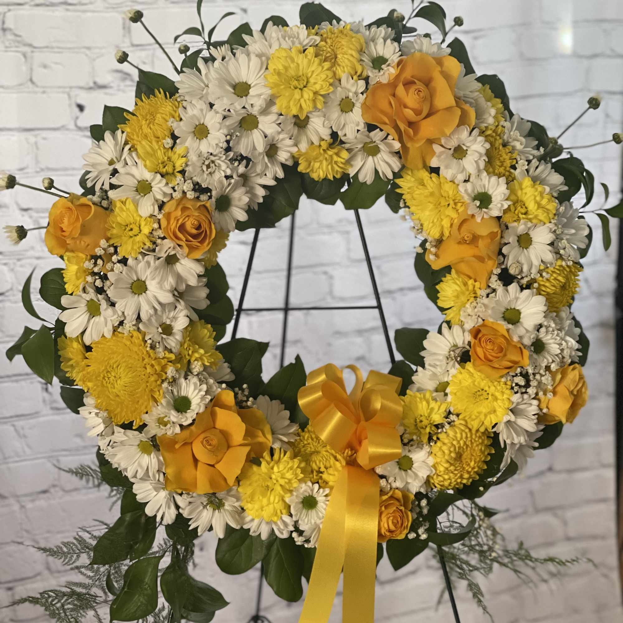 Yellow and white floral wreath with orange roses on a stand