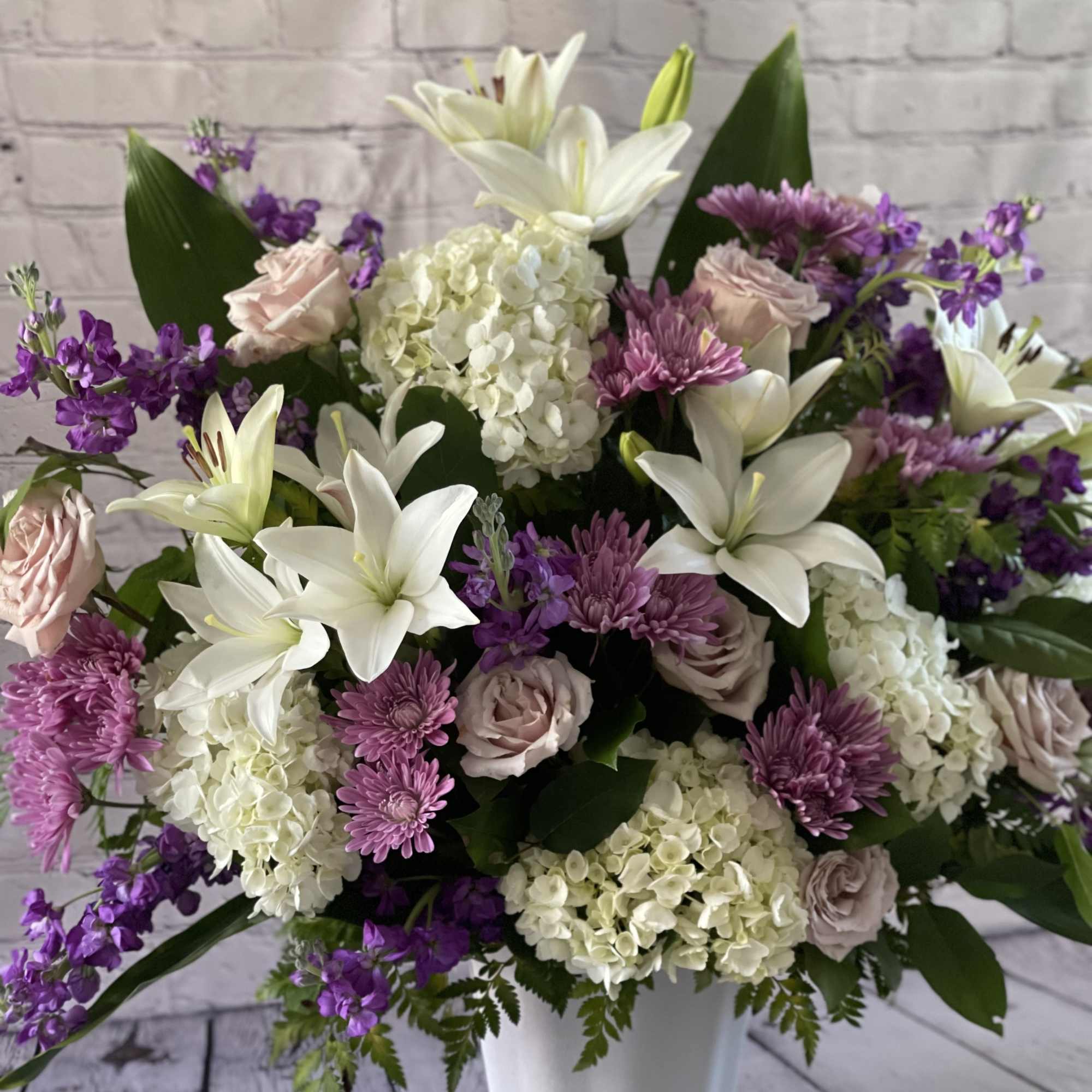 White lilies, hydrangeas, and purple flowers in a white vase