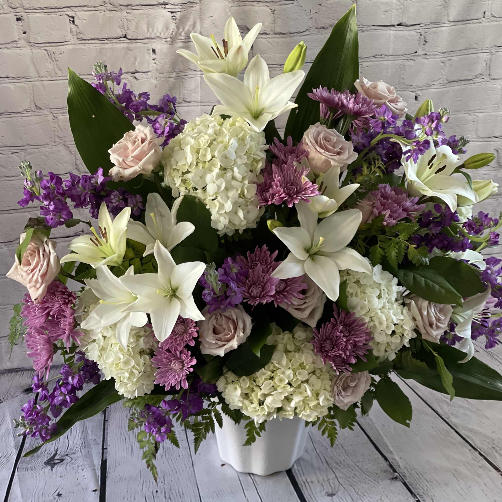 Large bouquet of white lilies, pink roses, and purple flowers in a white vase