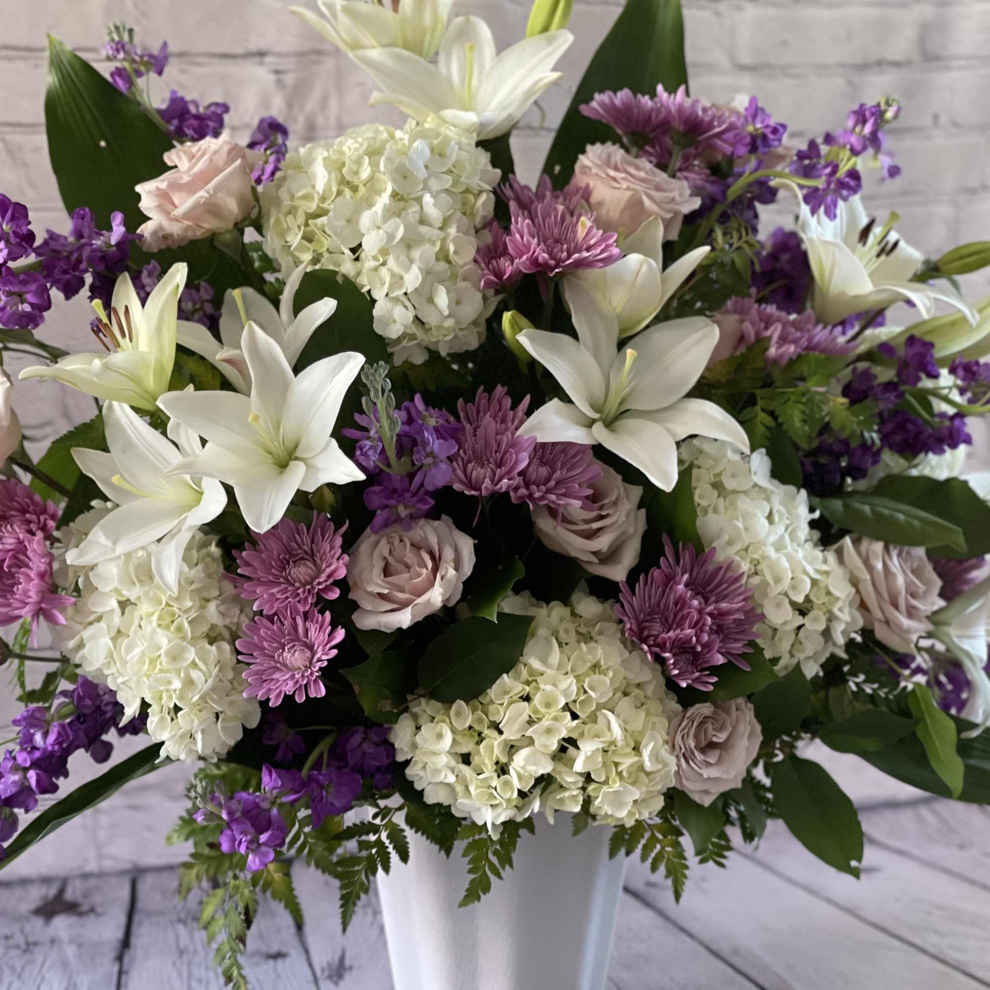 Bouquet of white lilies, pink roses, and purple flowers in a white vase
