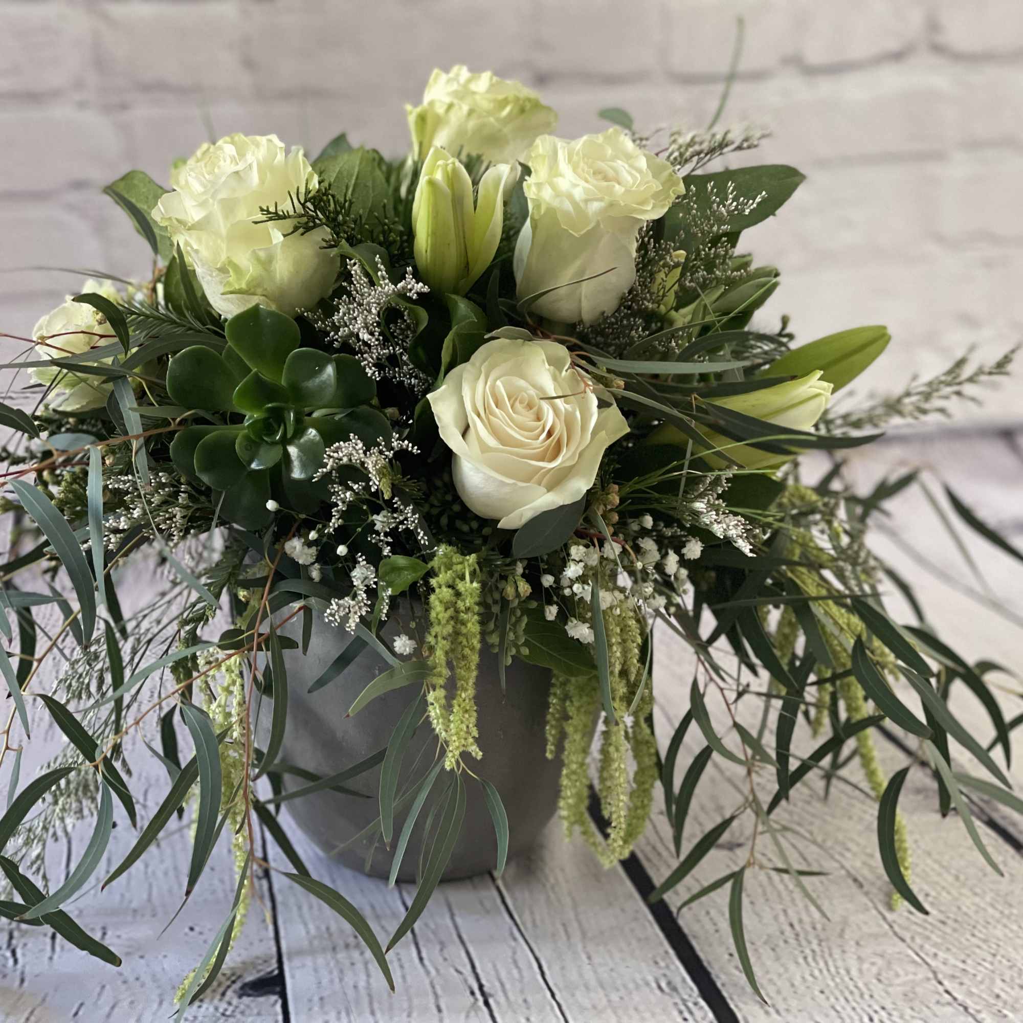White roses and lilies in a gray vase with trailing greenery