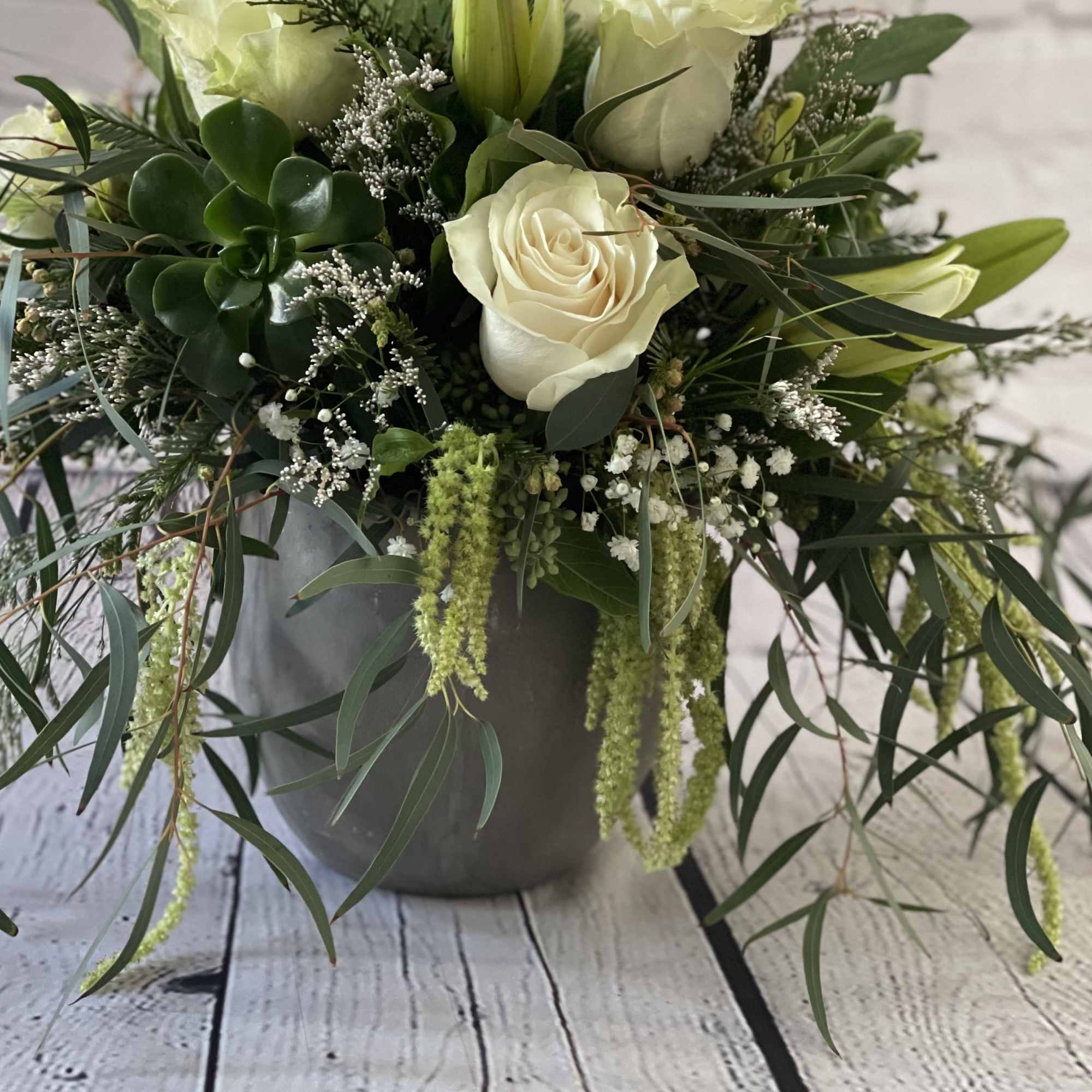 White roses and lilies in a gray pot with trailing greenery