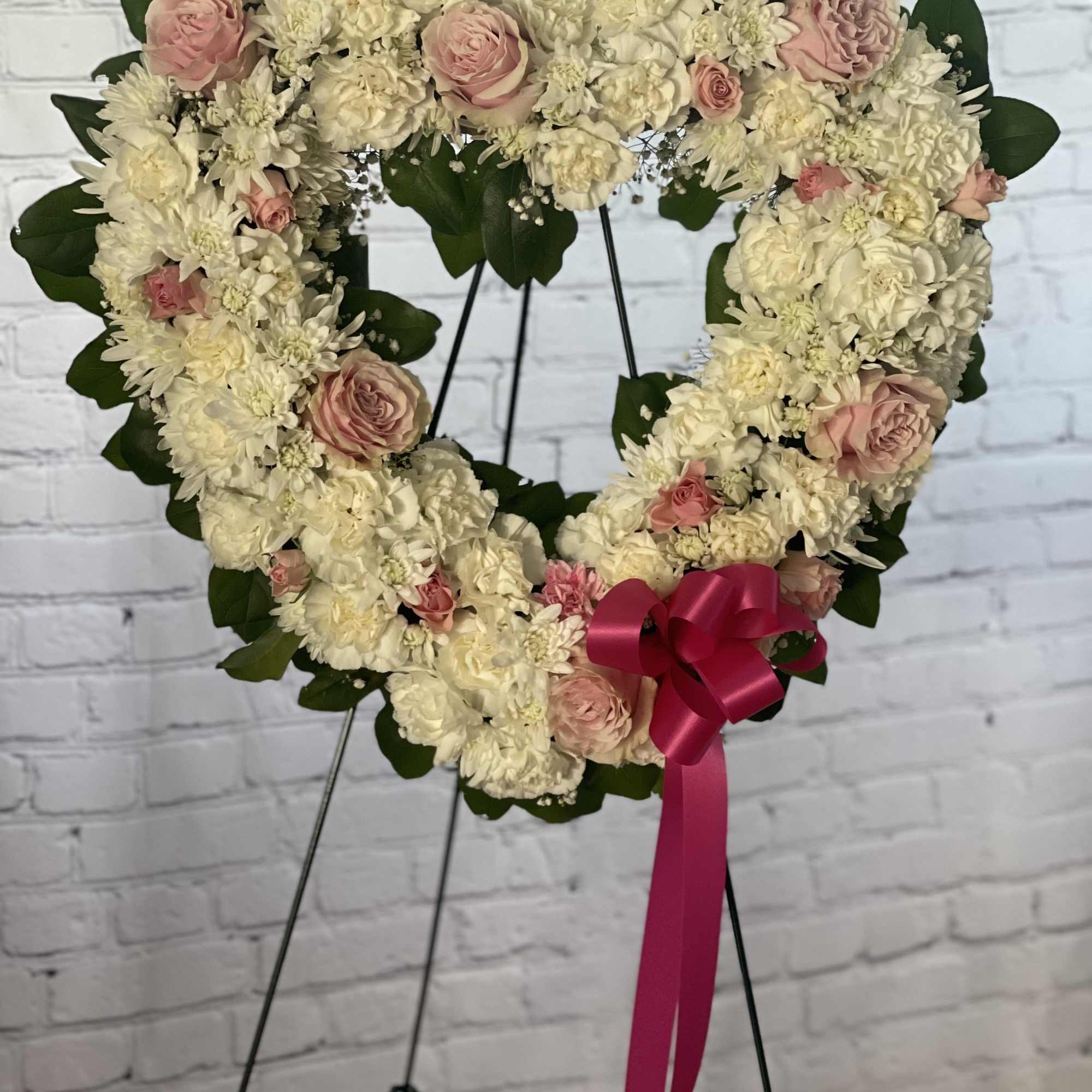 Heart-shaped floral wreath with cream and pink flowers on a stand