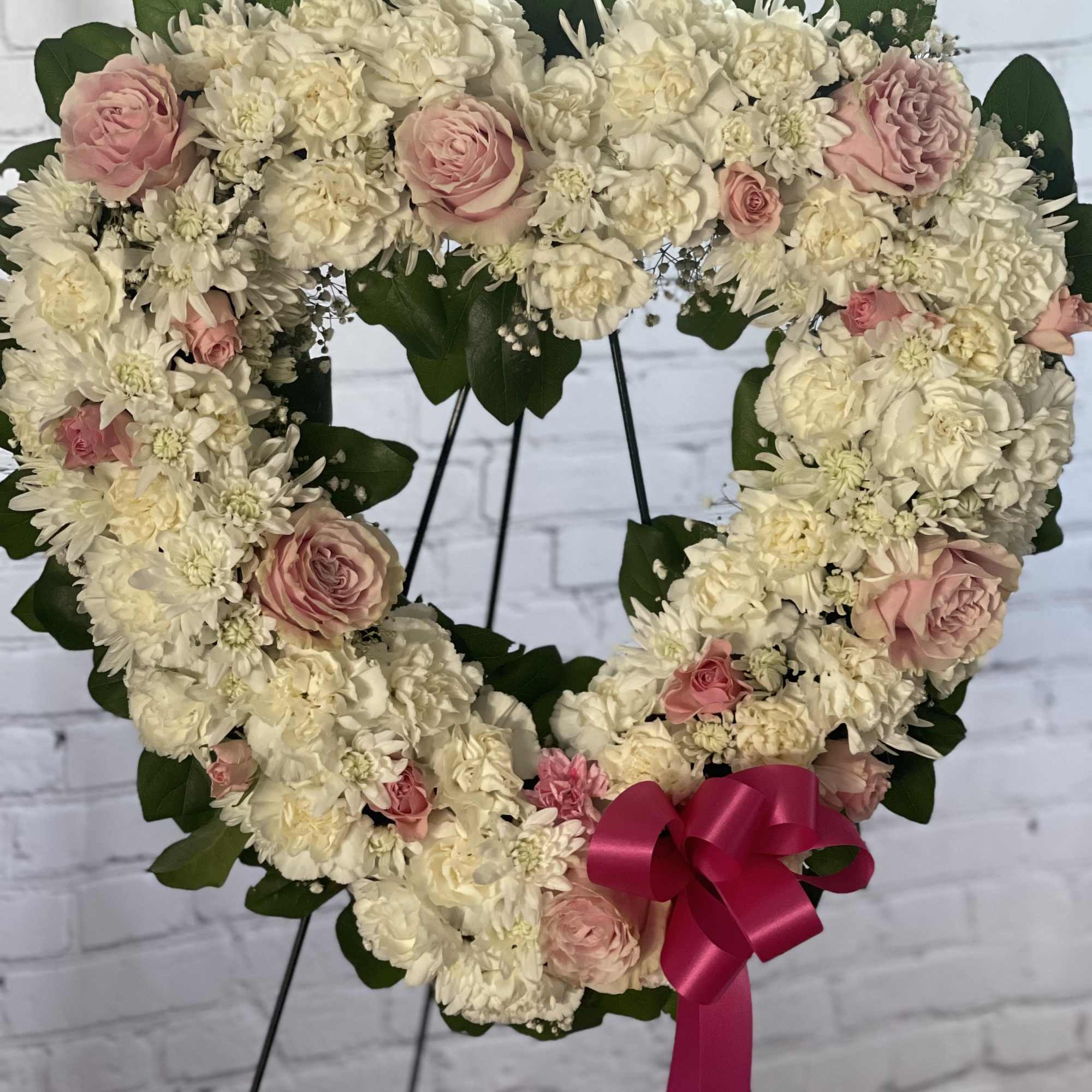Heart-shaped floral wreath of white and pink flowers with a ribbon bow
