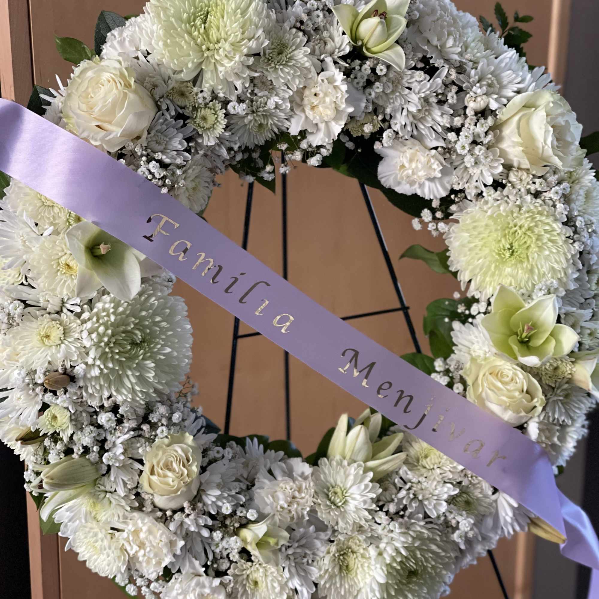 White floral wreath with a lavender ribbon on a stand