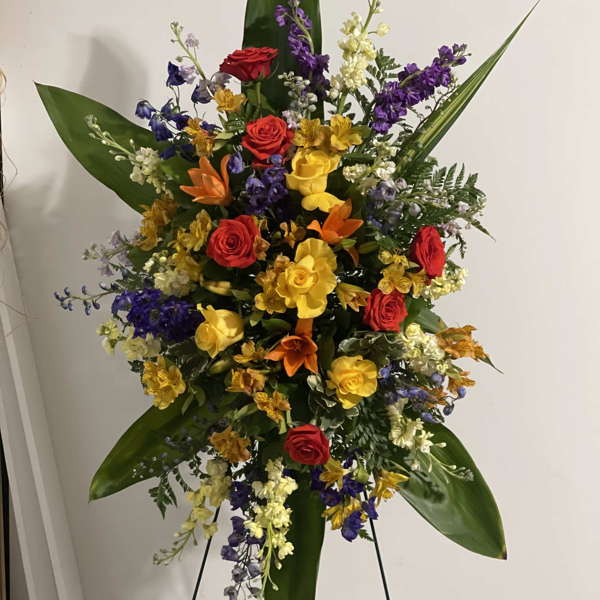 Tall standing arrangement of red, yellow, orange, and purple flowers on an easel