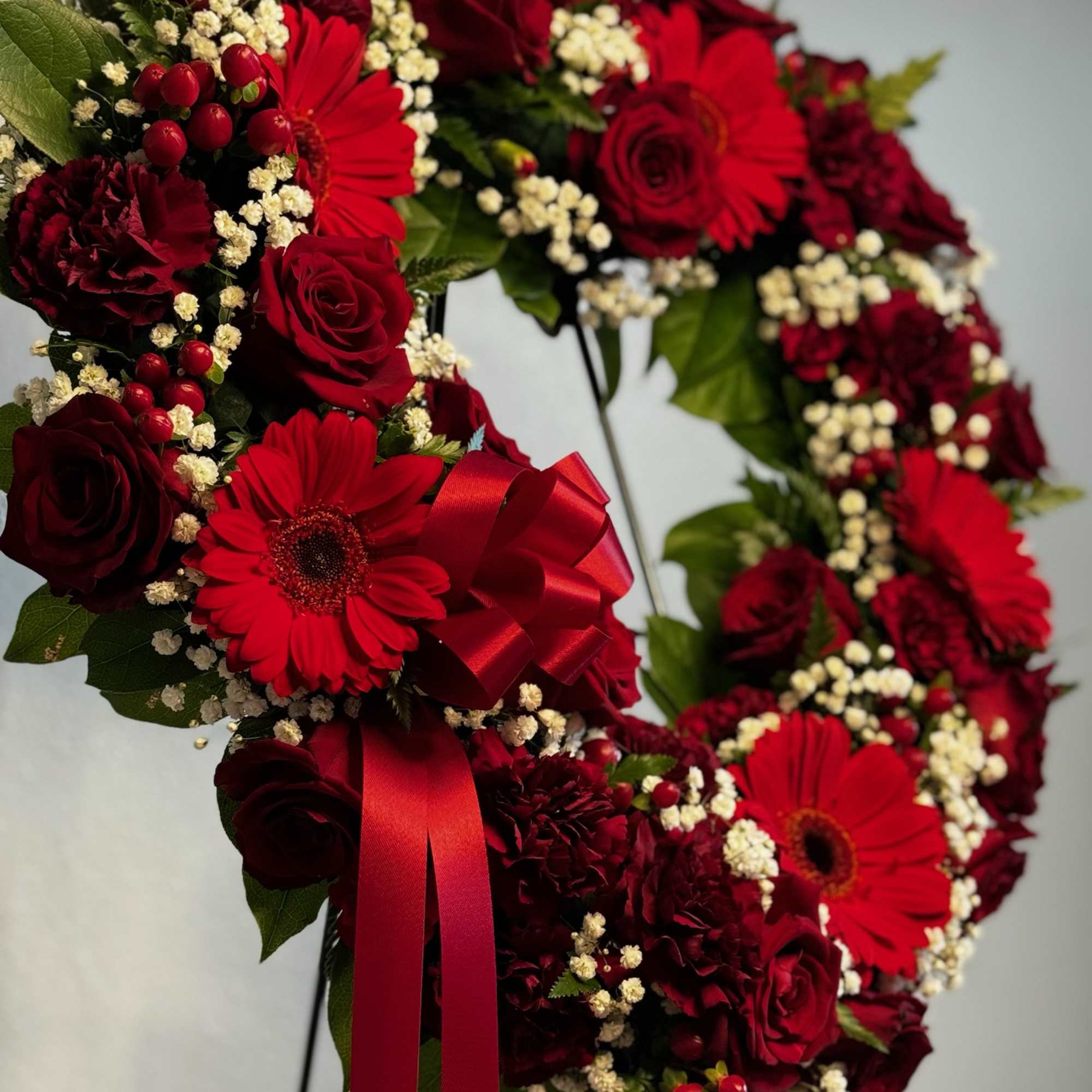 Red floral wreath with roses and gerbera daisies on a stand