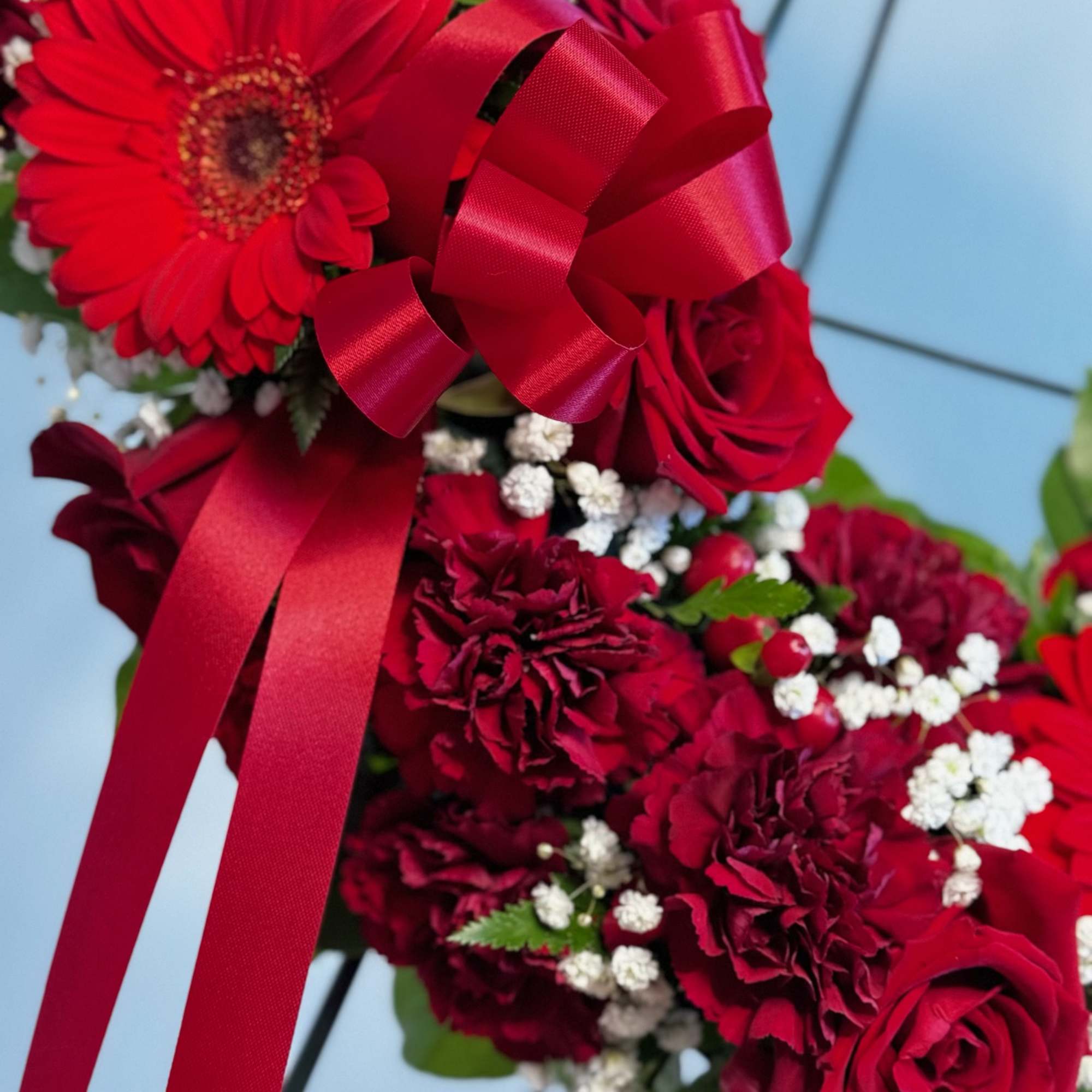 Red floral arrangement with roses, gerbera daisies, and ribbon