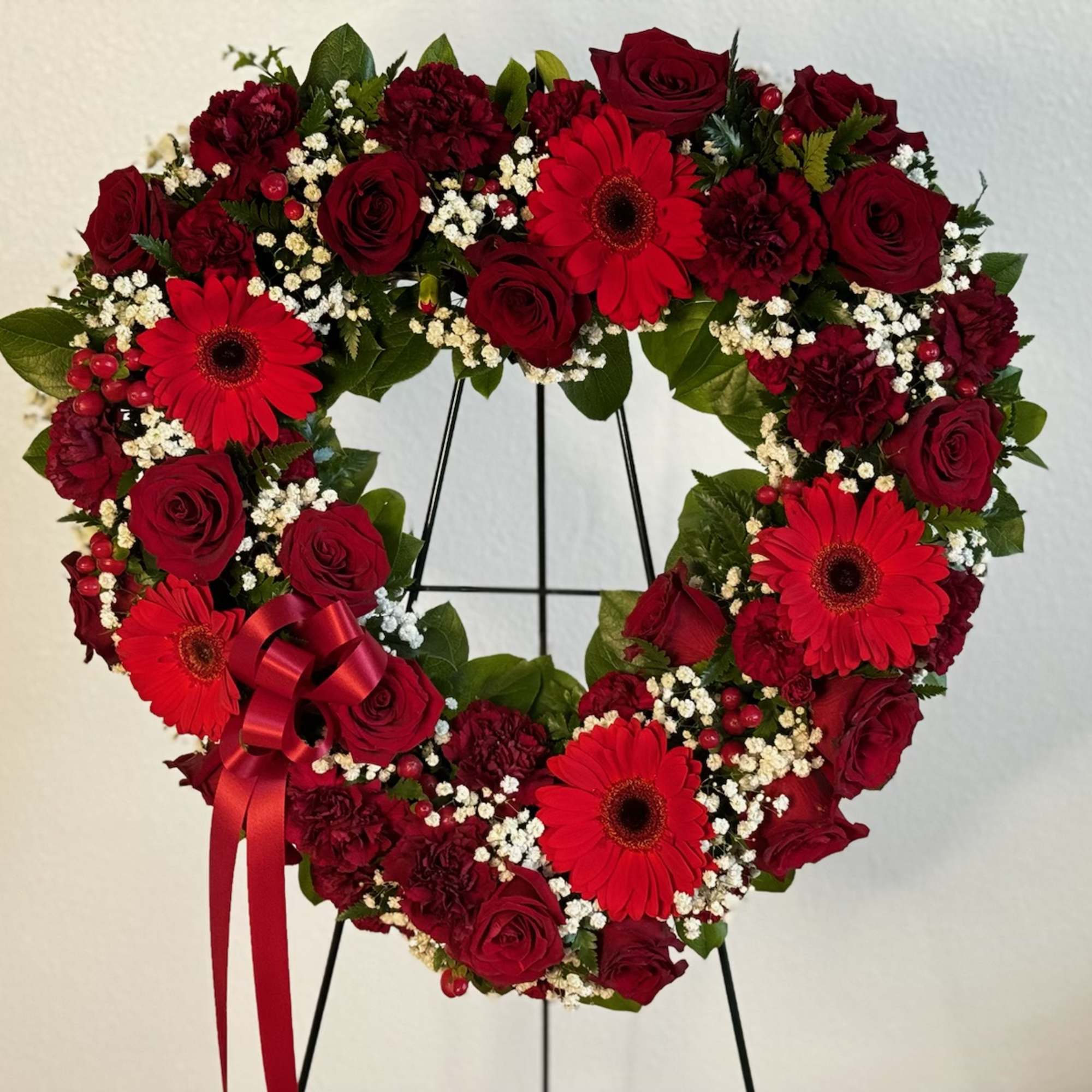 Heart-shaped wreath of red roses and gerbera daisies with a red ribbon