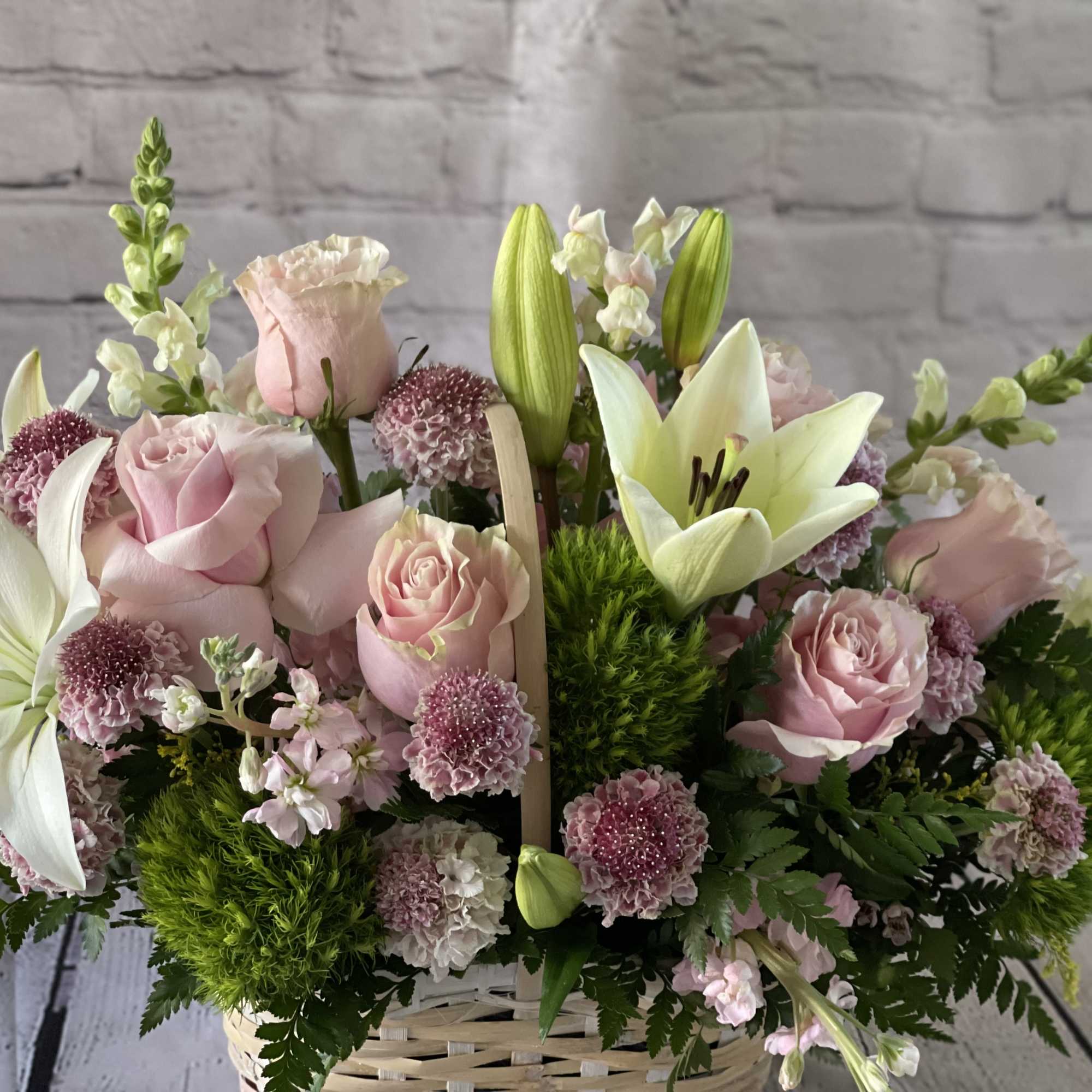 Basket arrangement of pink roses and white lilies with small purple blooms