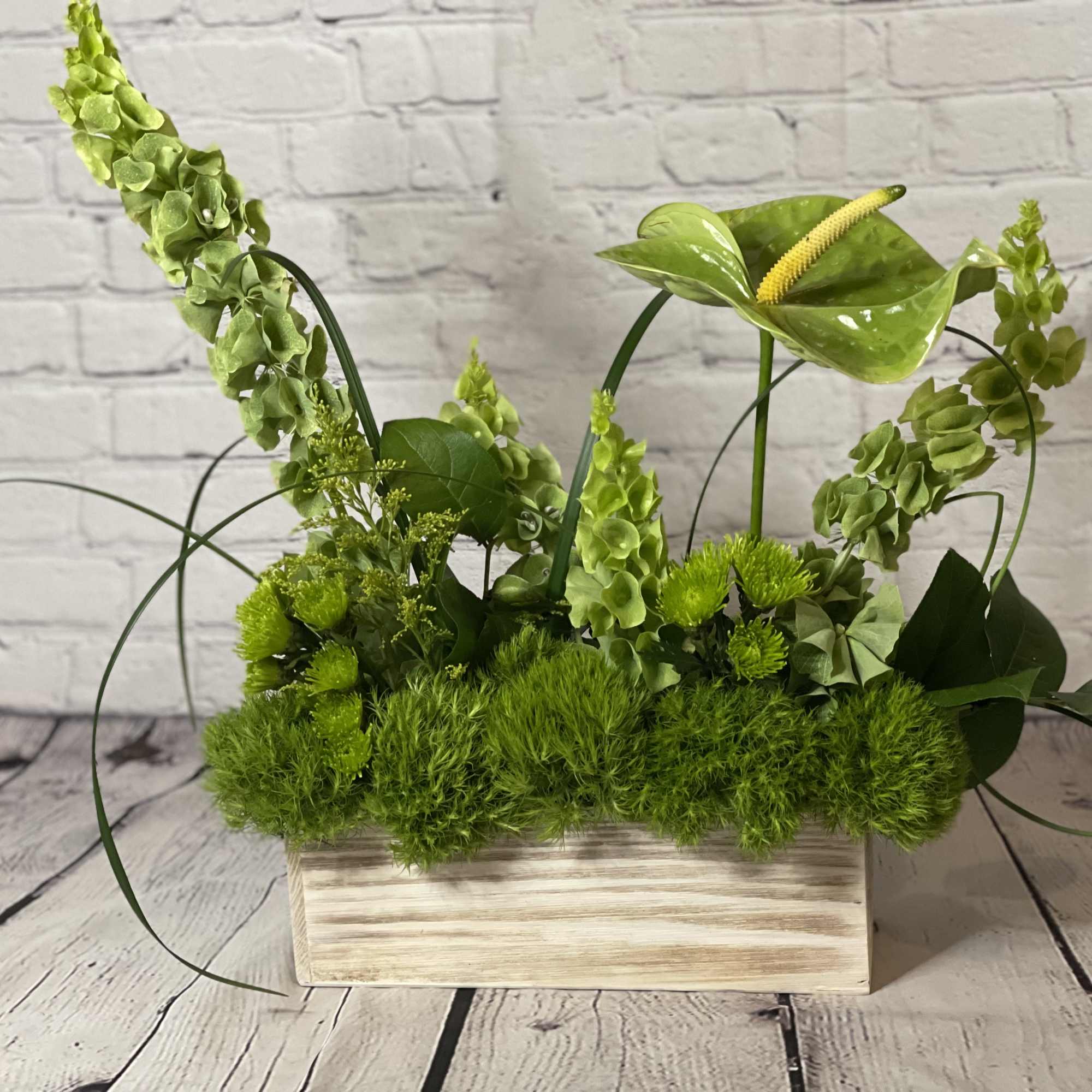 Green floral arrangement in a rectangular wooden planter with anthurium and tall spikes