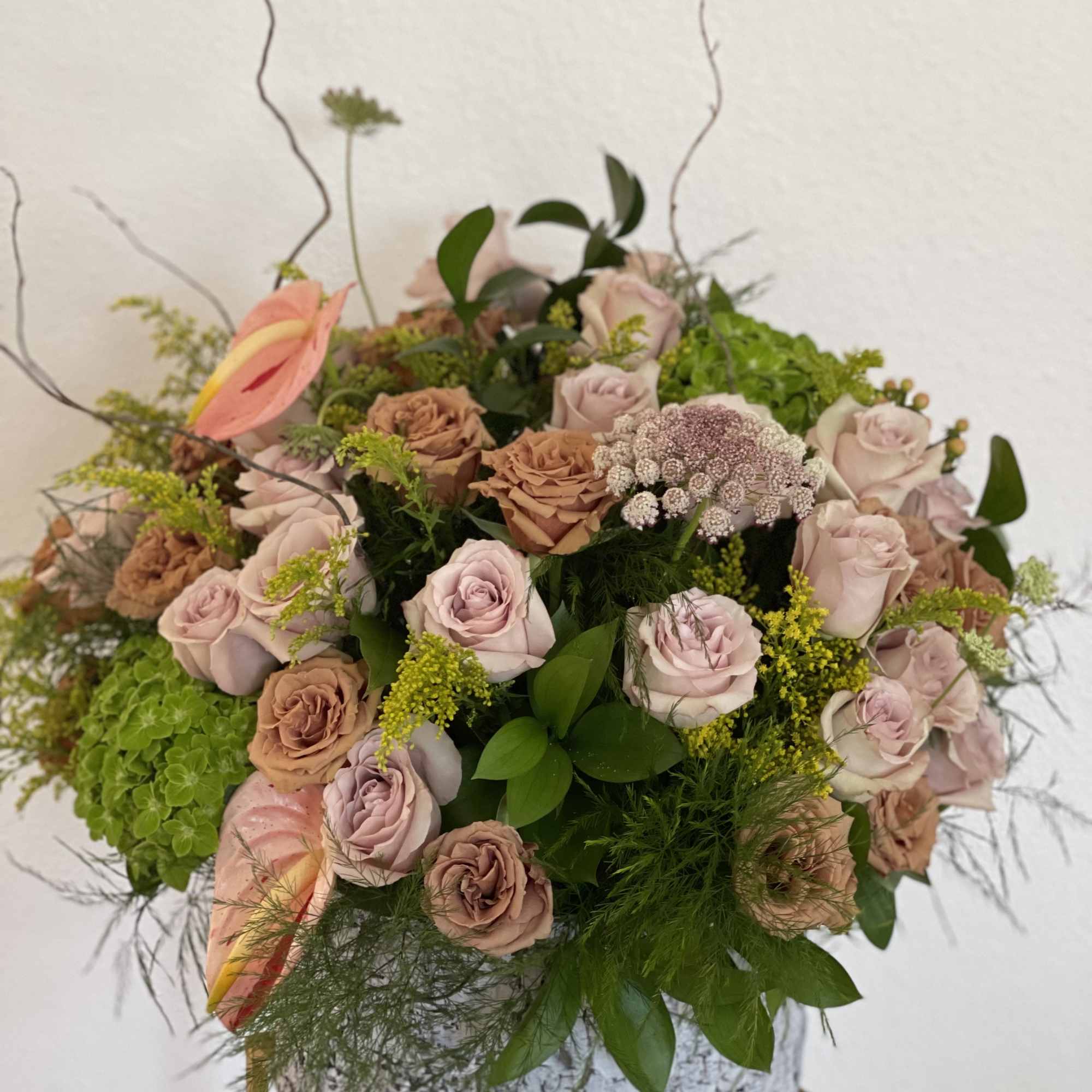 Large pastel rose arrangement in a silver container with greenery
