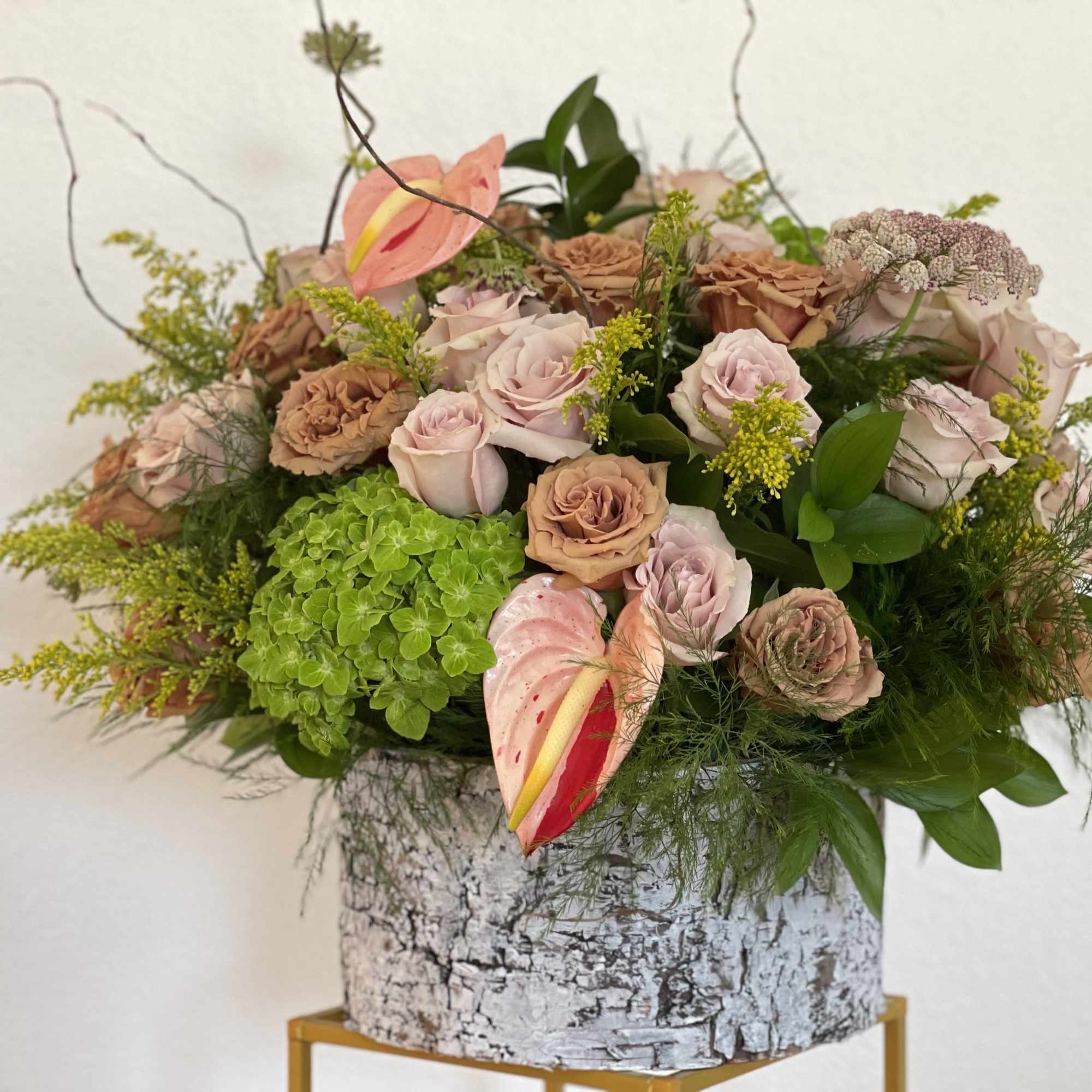 Pink and tan roses in a birch bark container with green hydrangea