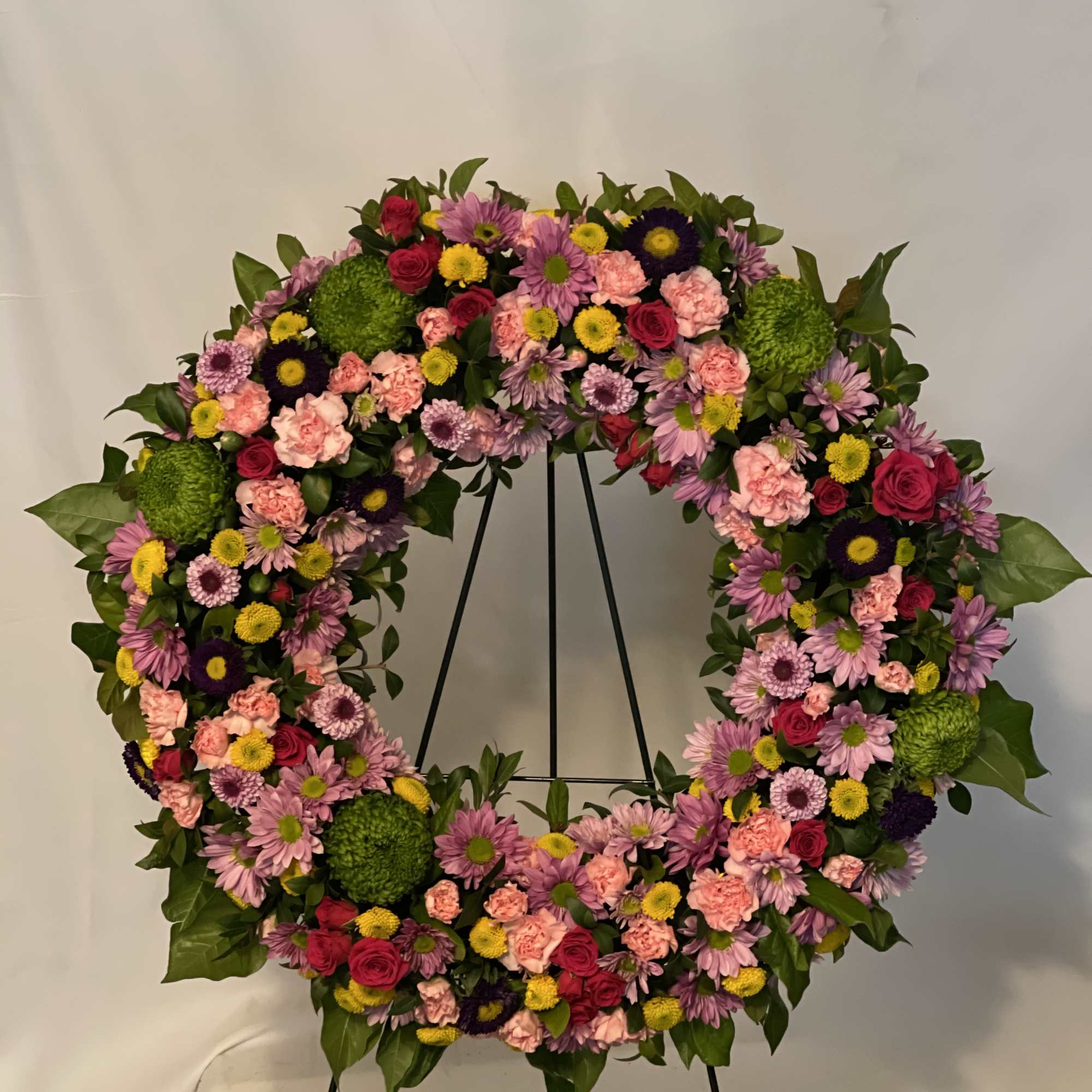 Circular floral wreath on a stand with pink, purple, yellow, and green blooms