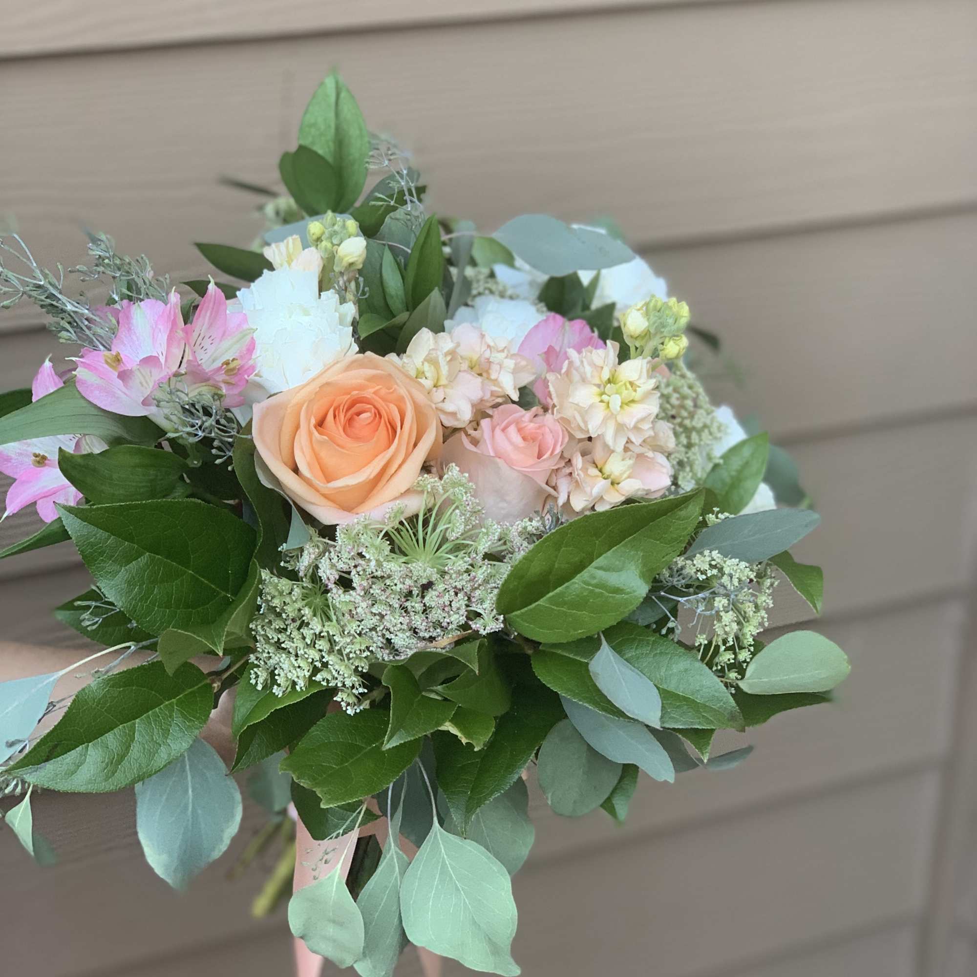 Hand-tied bouquet of peach and pink roses with mixed greenery