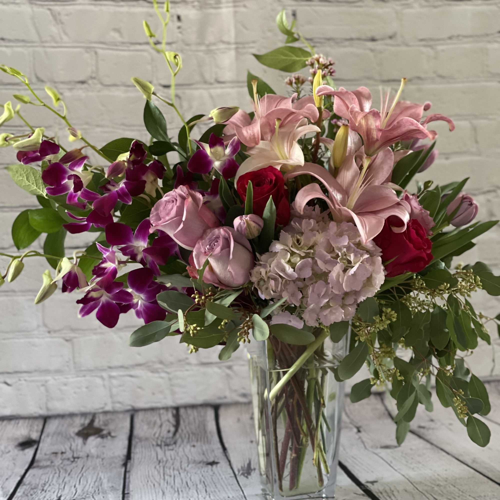 Pink lilies and roses in a clear glass vase with purple orchids