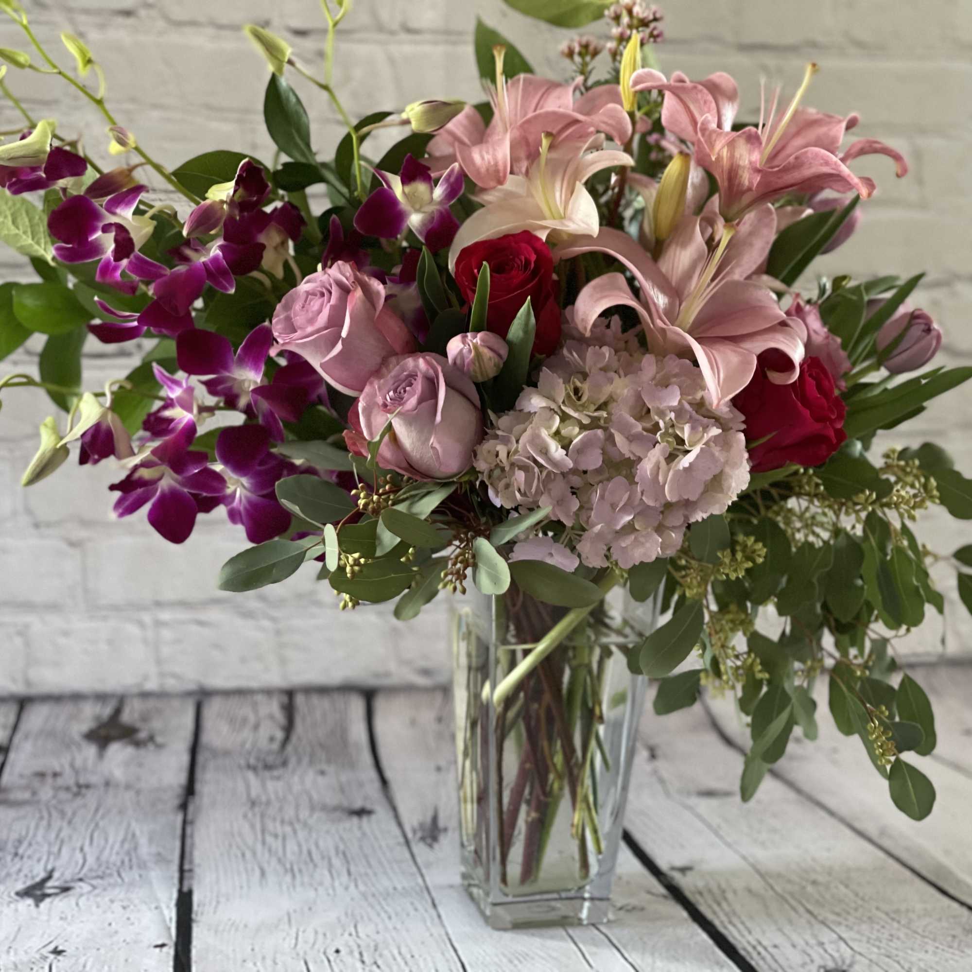 Bouquet of pink lilies, roses, orchids, and hydrangea in a clear glass vase