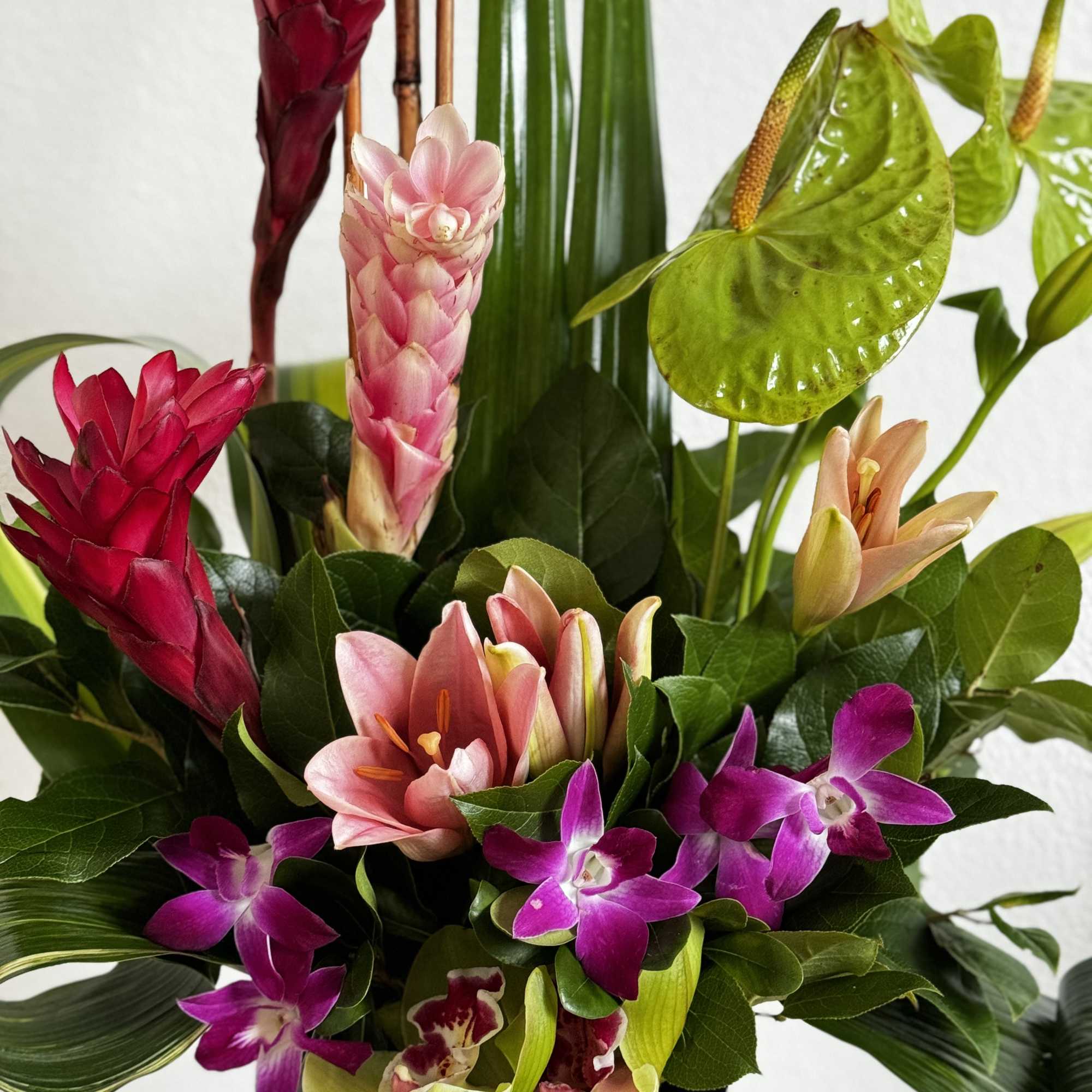 Tall tropical arrangement with pink lilies, purple orchids, and green anthuriums in a black vase