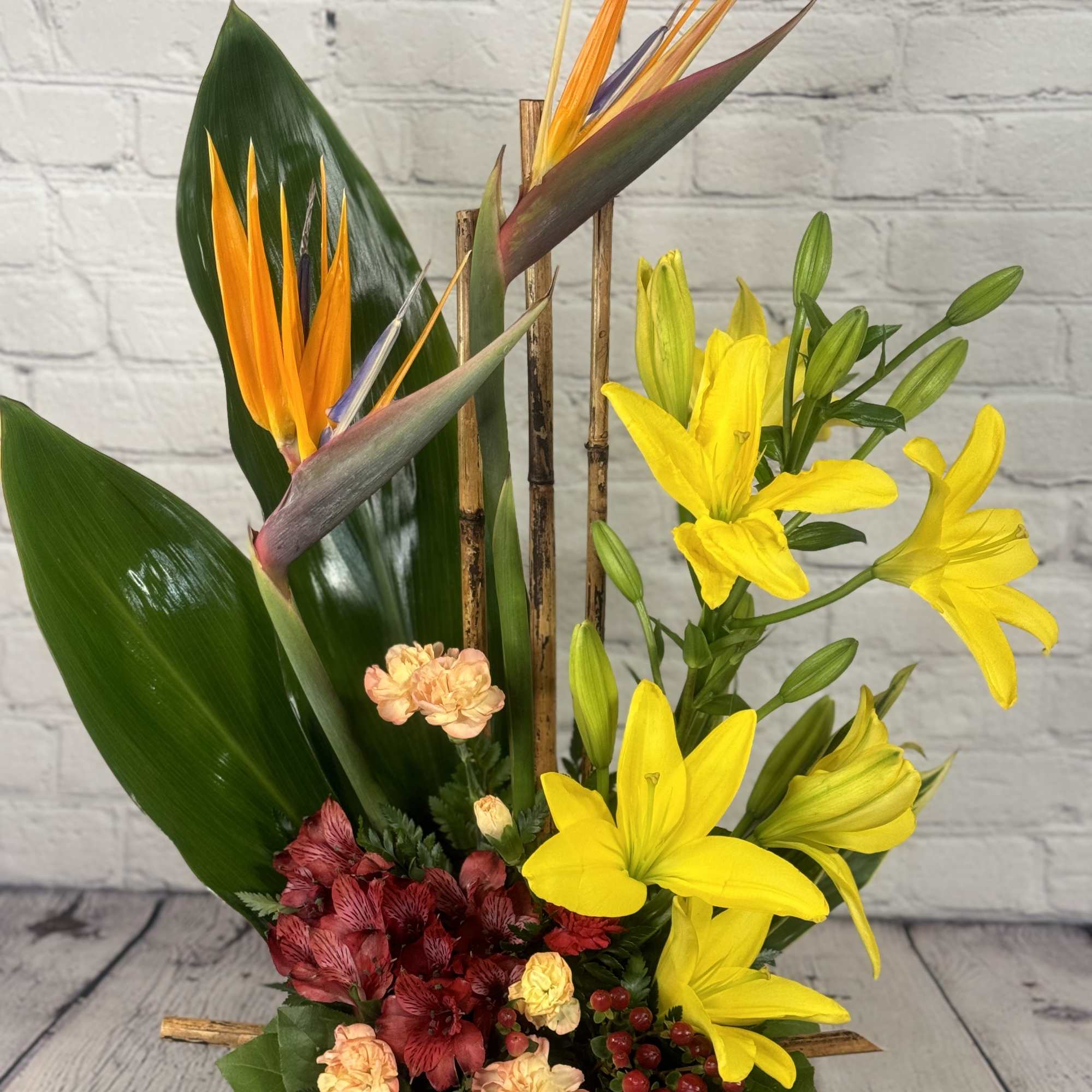 Tropical flower arrangement with yellow lilies and bird of paradise in a black container, photo 2 of 4