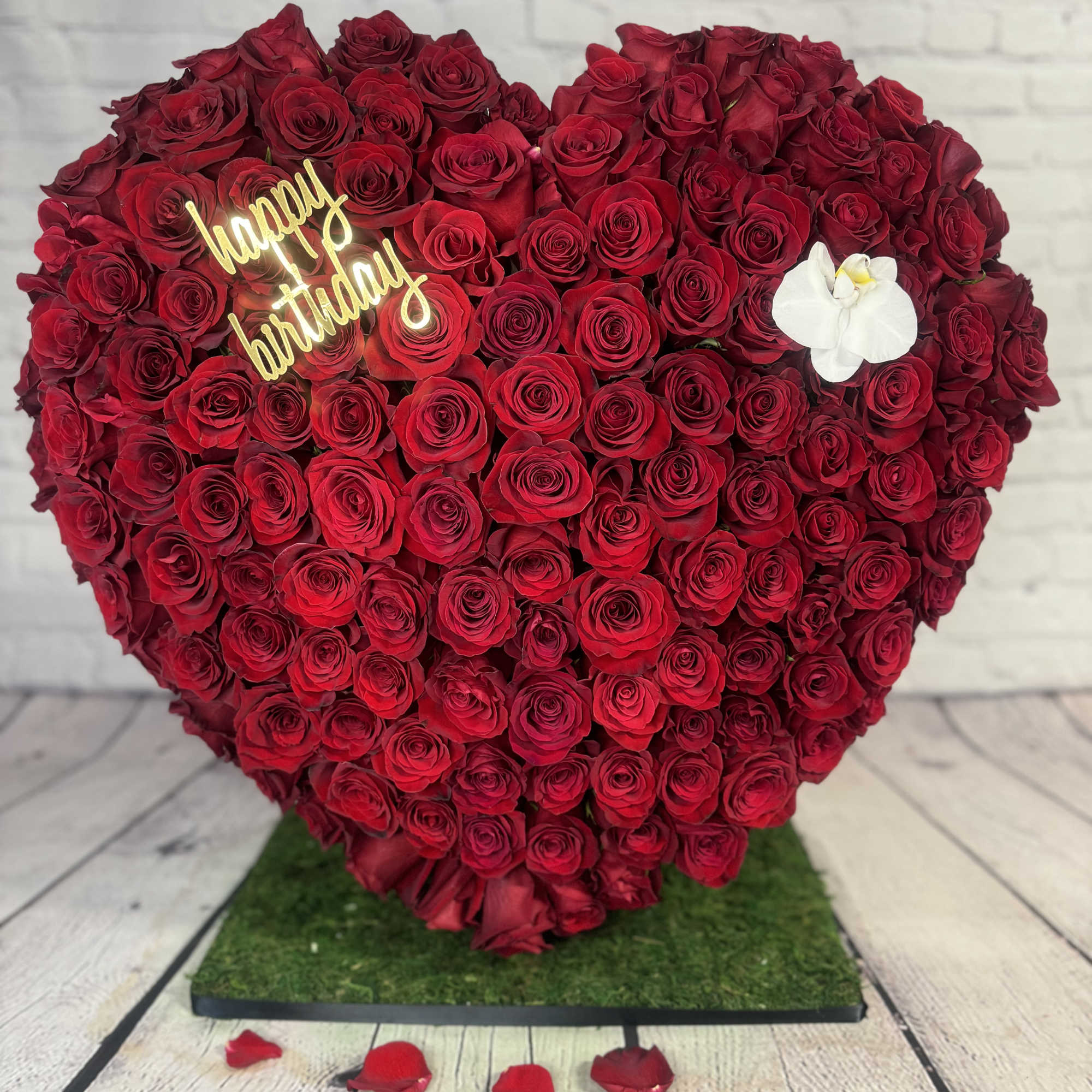Heart-shaped red rose arrangement with a happy birthday sign and white orchid