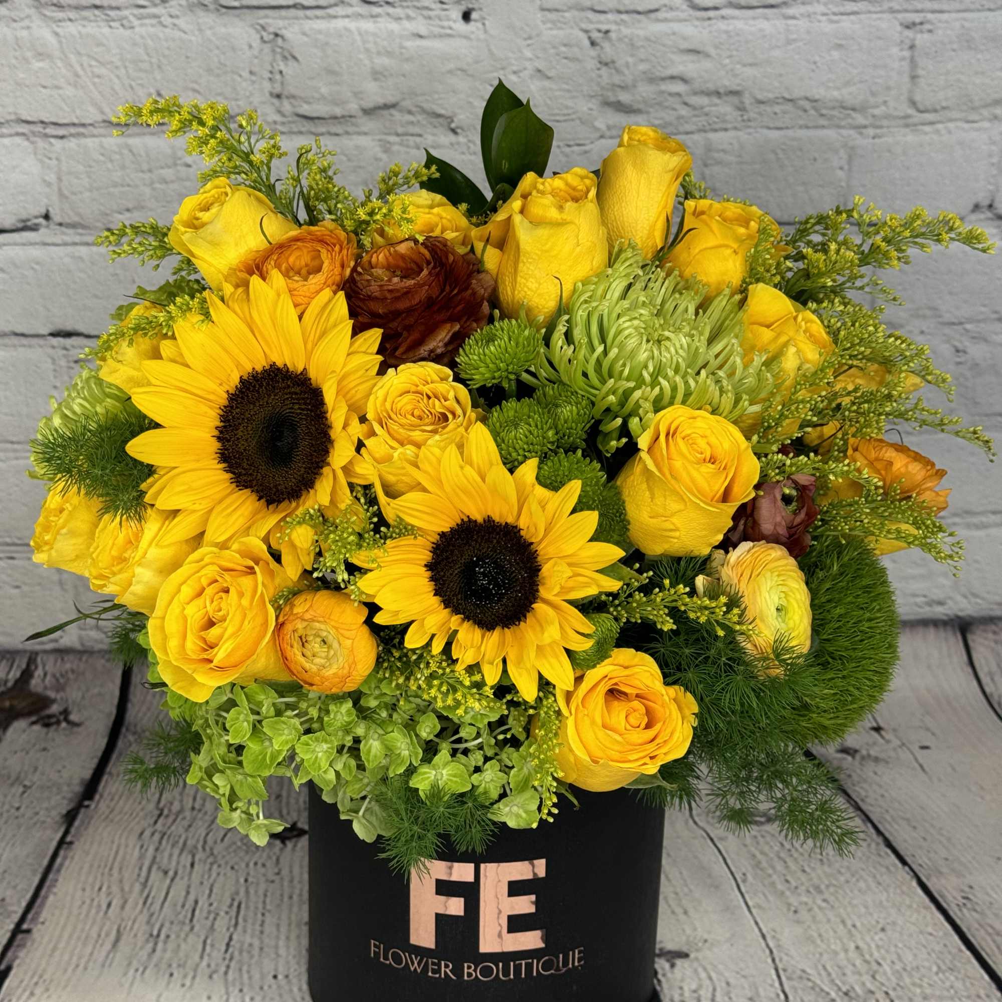 Yellow roses and sunflowers arranged in a black hatbox