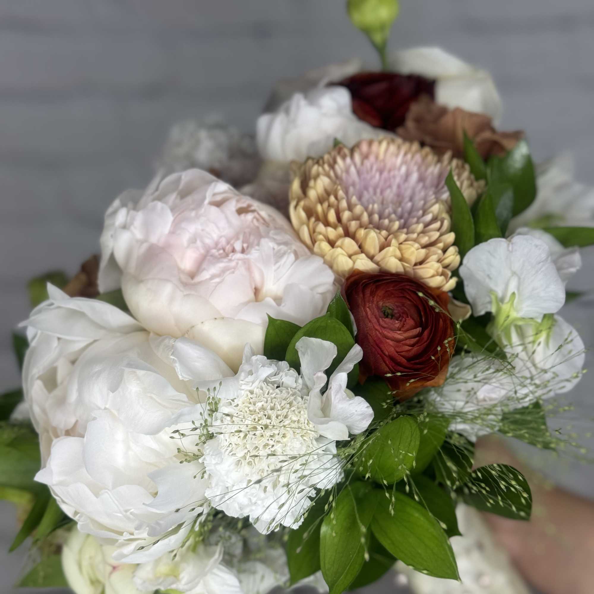 Bouquet of white and blush flowers with a red bloom and green accents