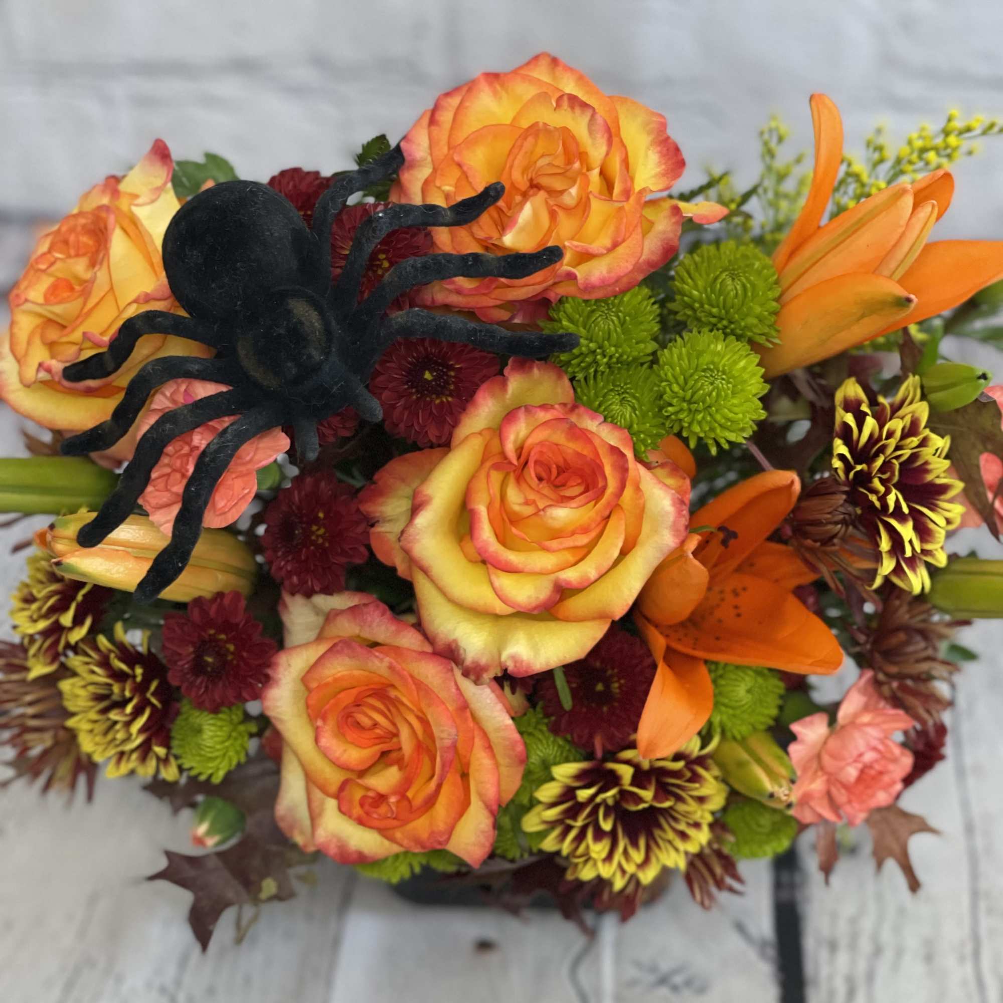 Colorful bouquet with orange roses, lilies, and a black spider decoration