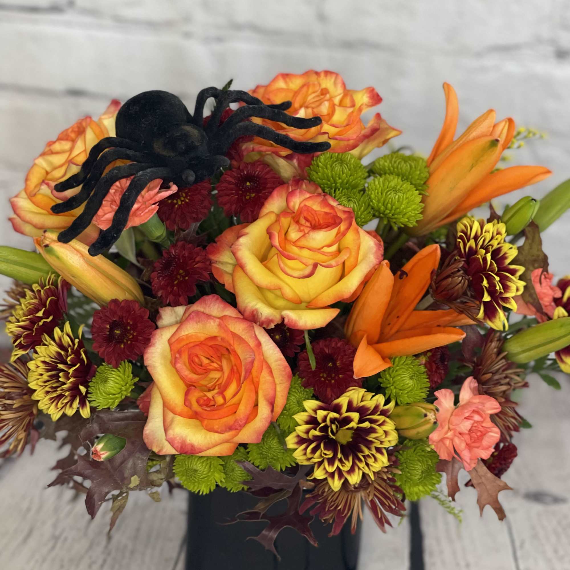 Orange and yellow floral arrangement with a black spider decoration in a black vase