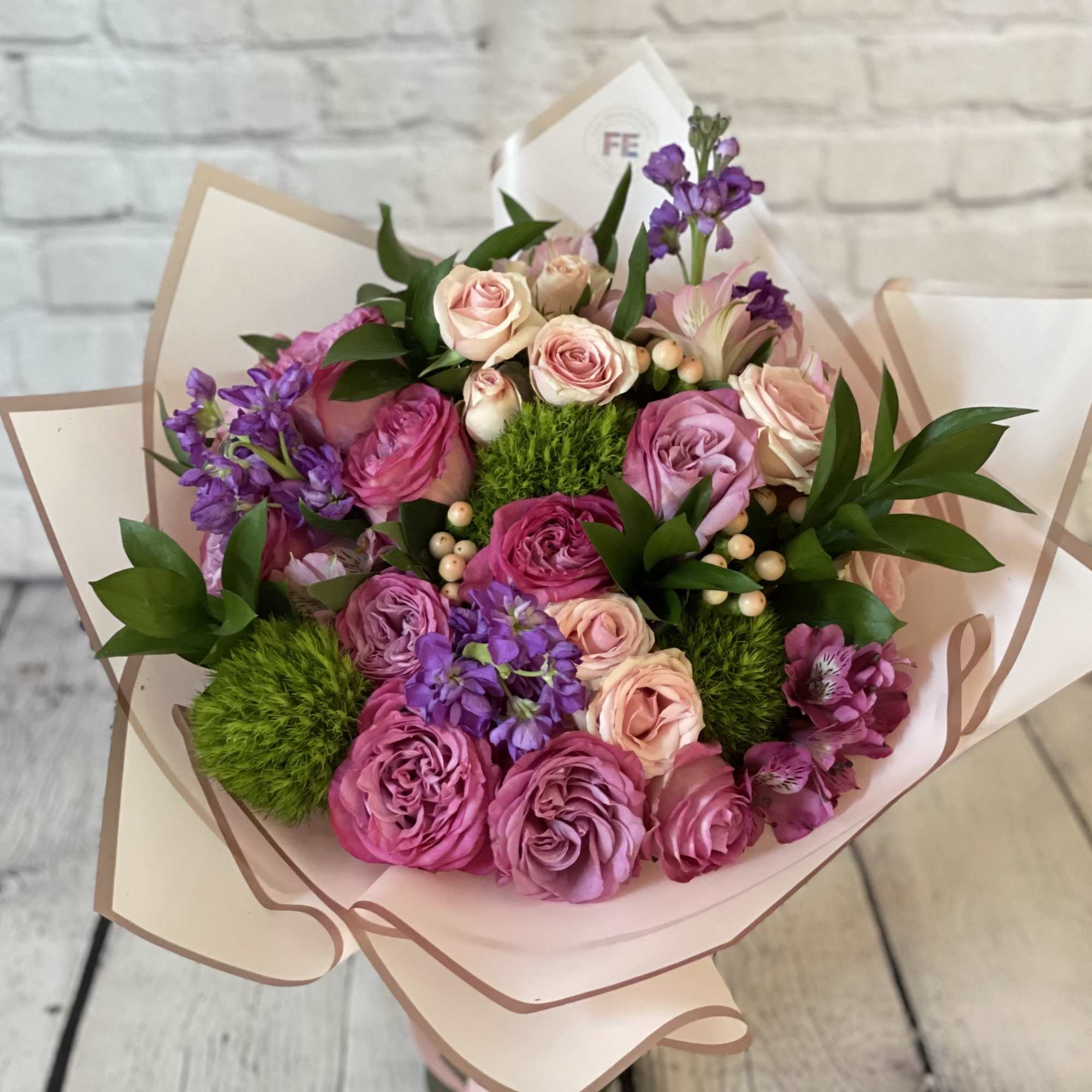 Bouquet of pink and purple roses with purple flowers wrapped in pale paper