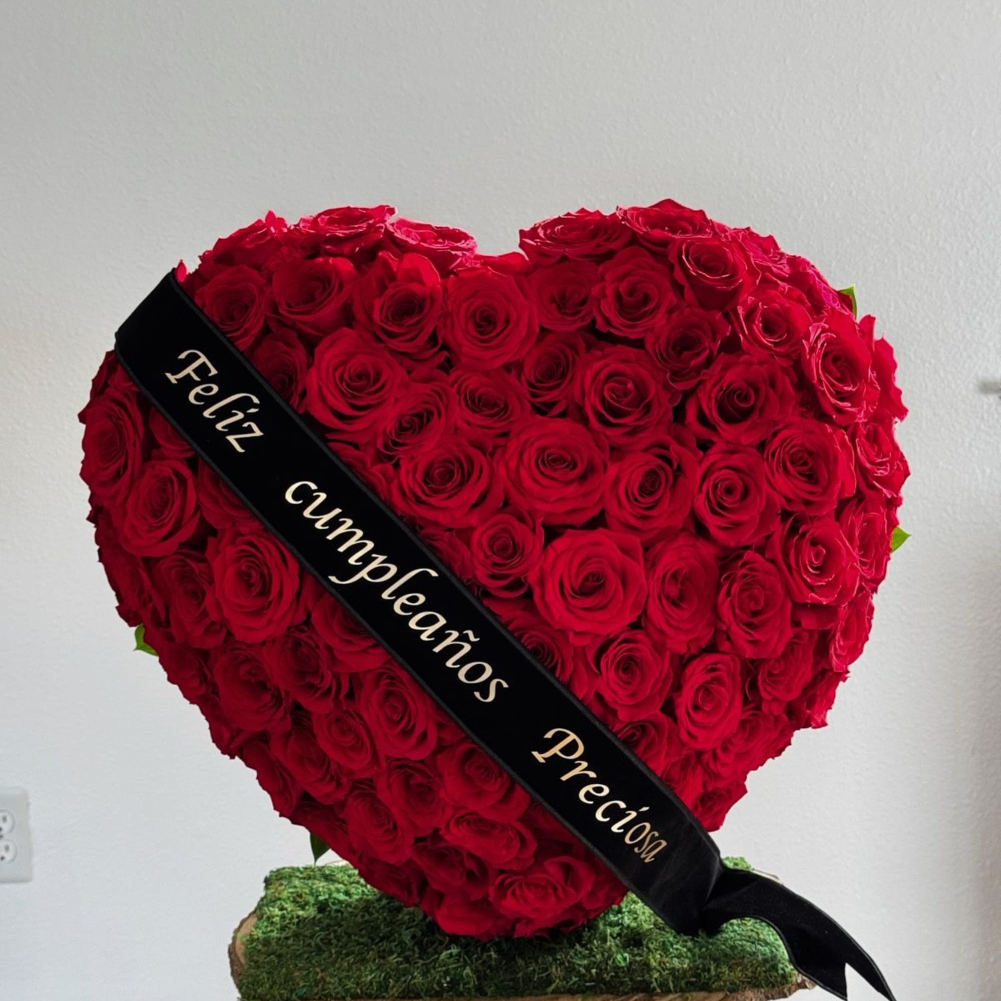 Heart-shaped red rose arrangement with a black ribbon on a moss-covered base