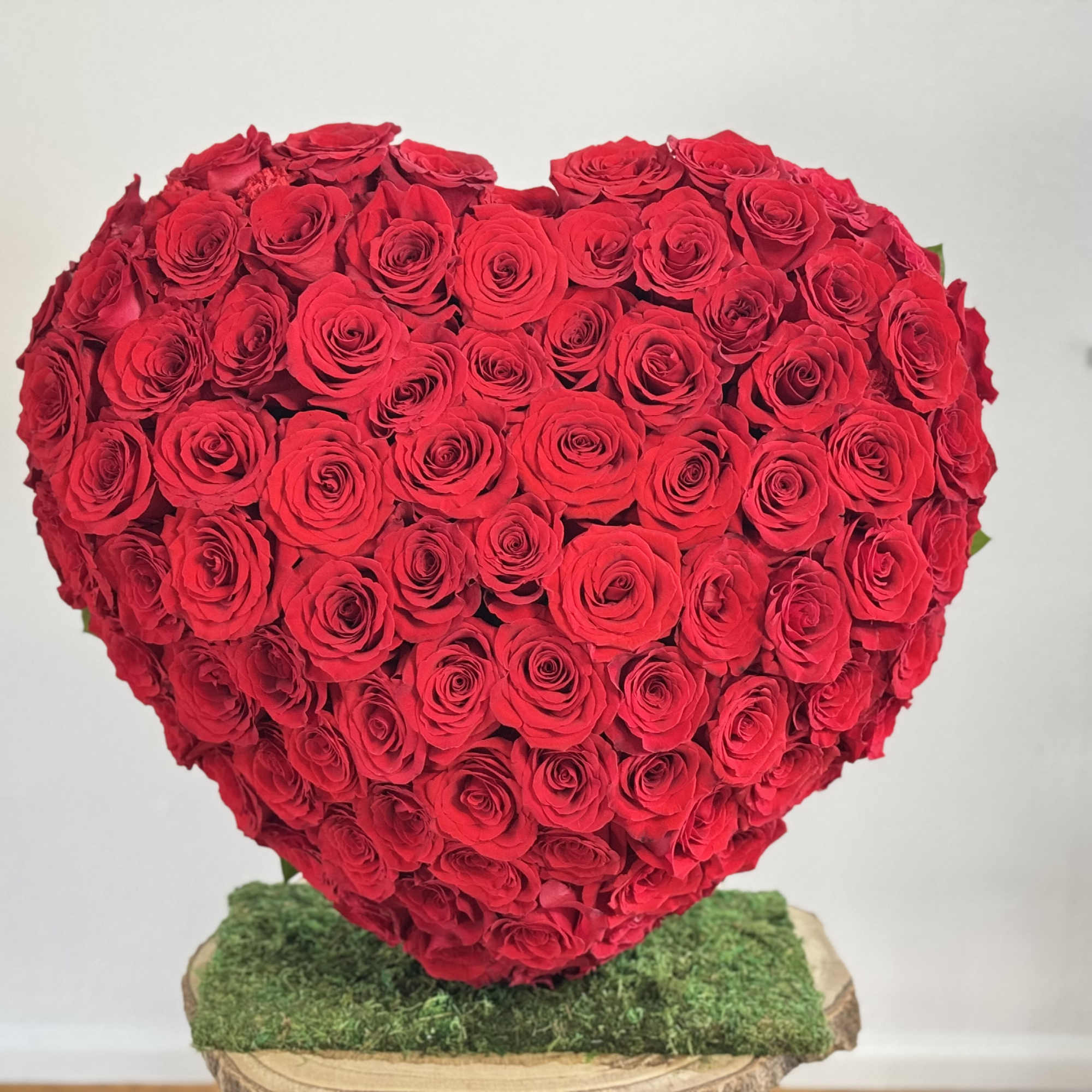 Heart-shaped arrangement of red roses on a moss-covered base