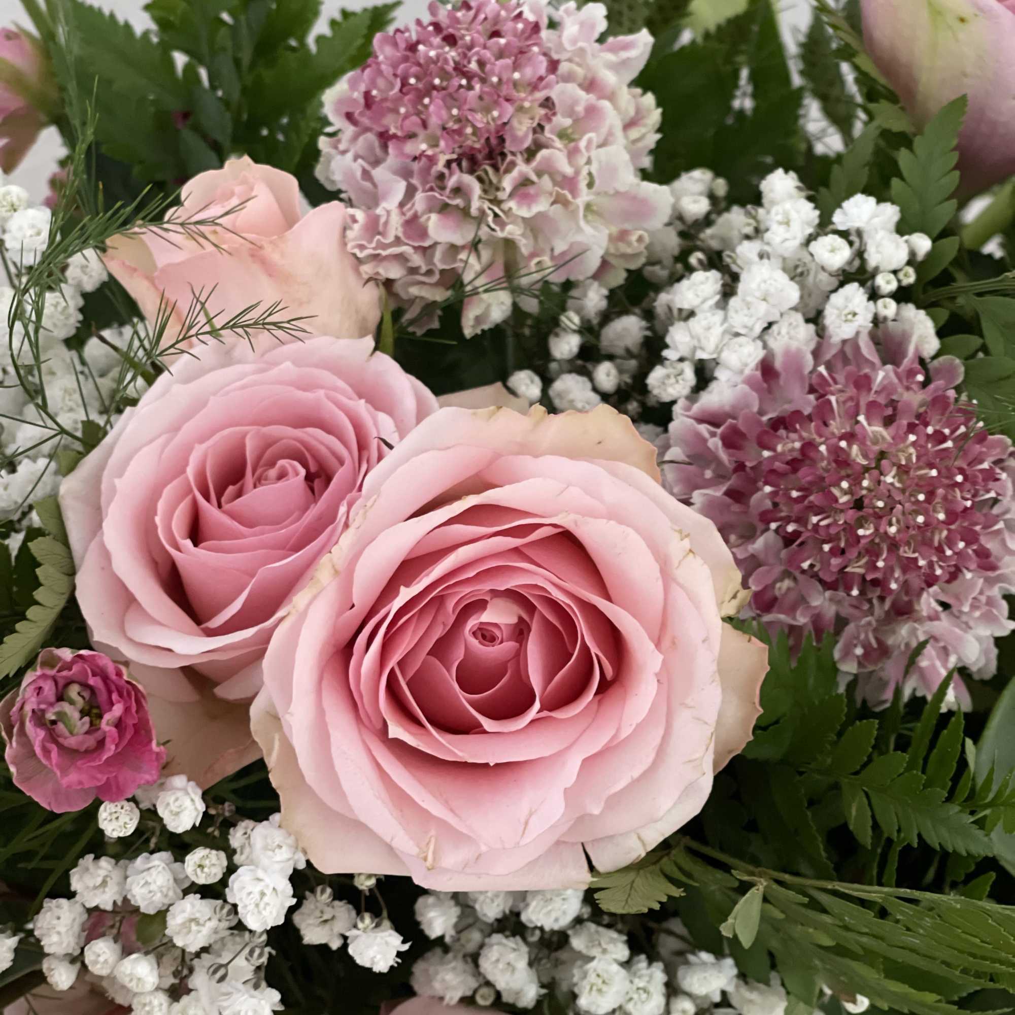 Pink roses with purple blooms and white filler flowers in a bouquet