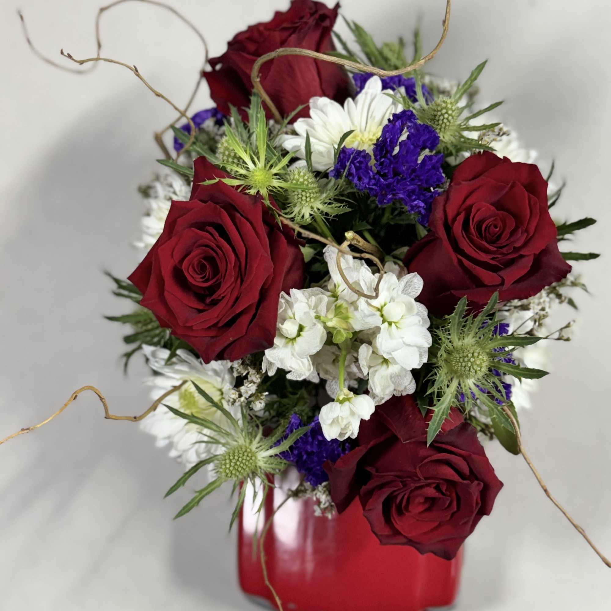 Red roses with white and purple flowers in a red vase