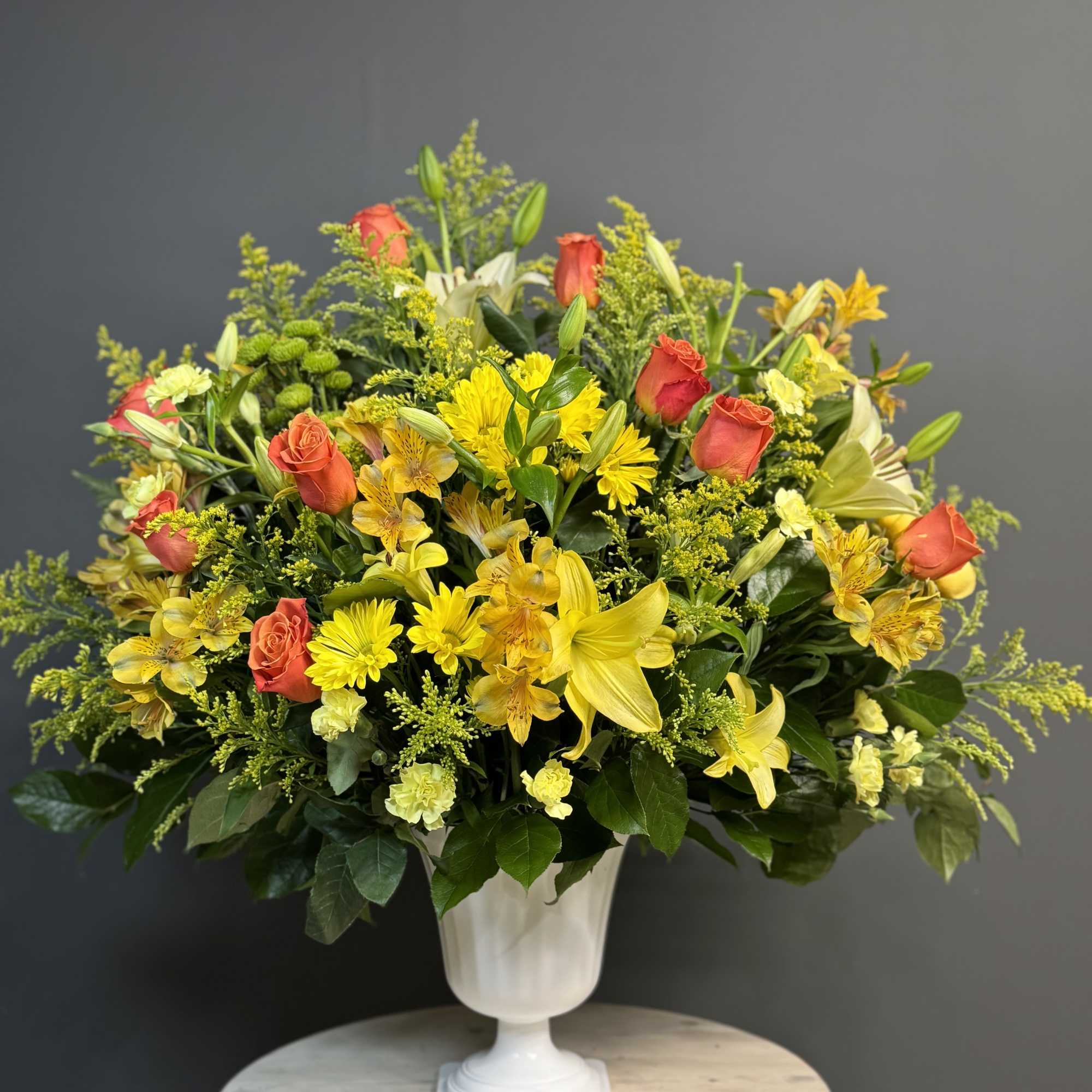 Yellow and coral mixed flower arrangement in a white pedestal vase