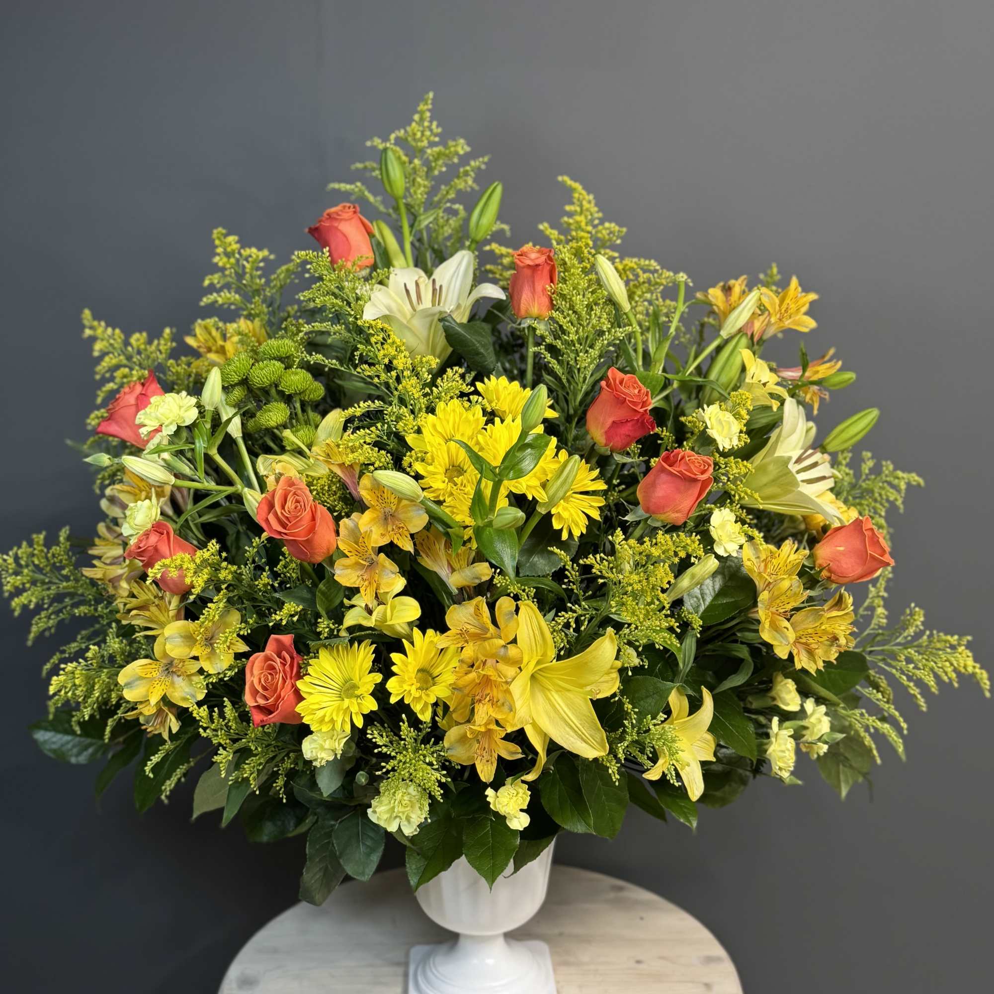 Yellow and orange mixed flower arrangement in a white pedestal vase