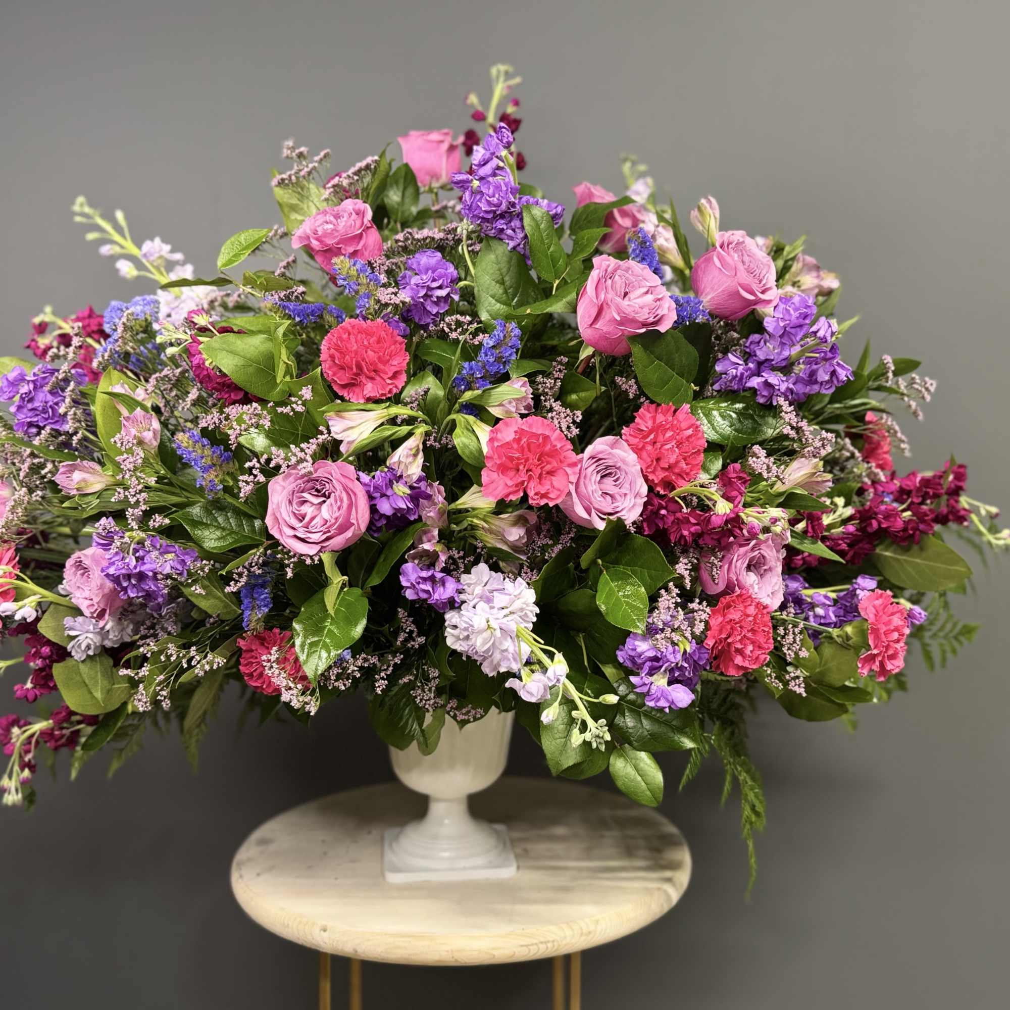 Large pink and purple floral arrangement in a white pedestal vase