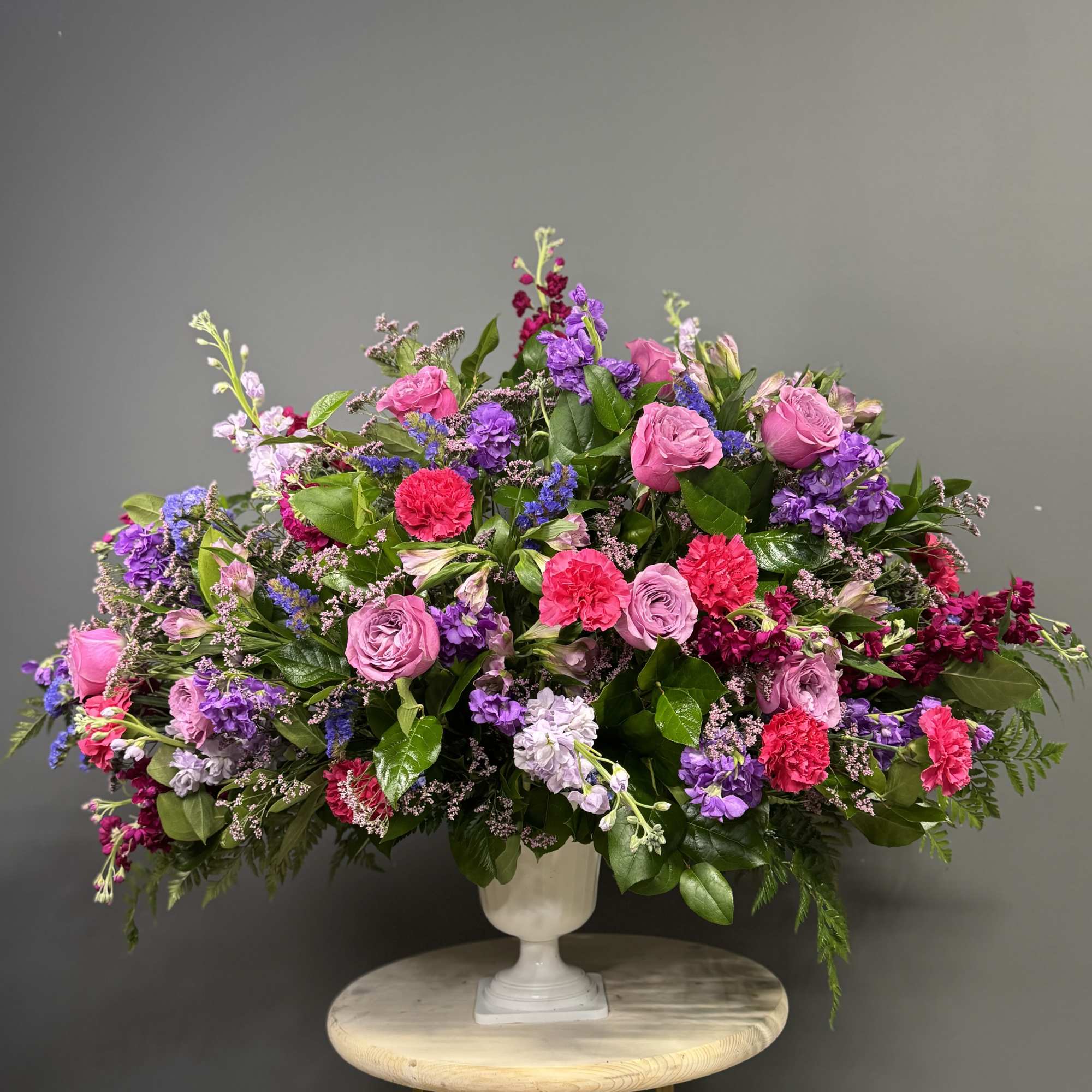 Large mixed bouquet of pink, purple, and red flowers in a white urn vase