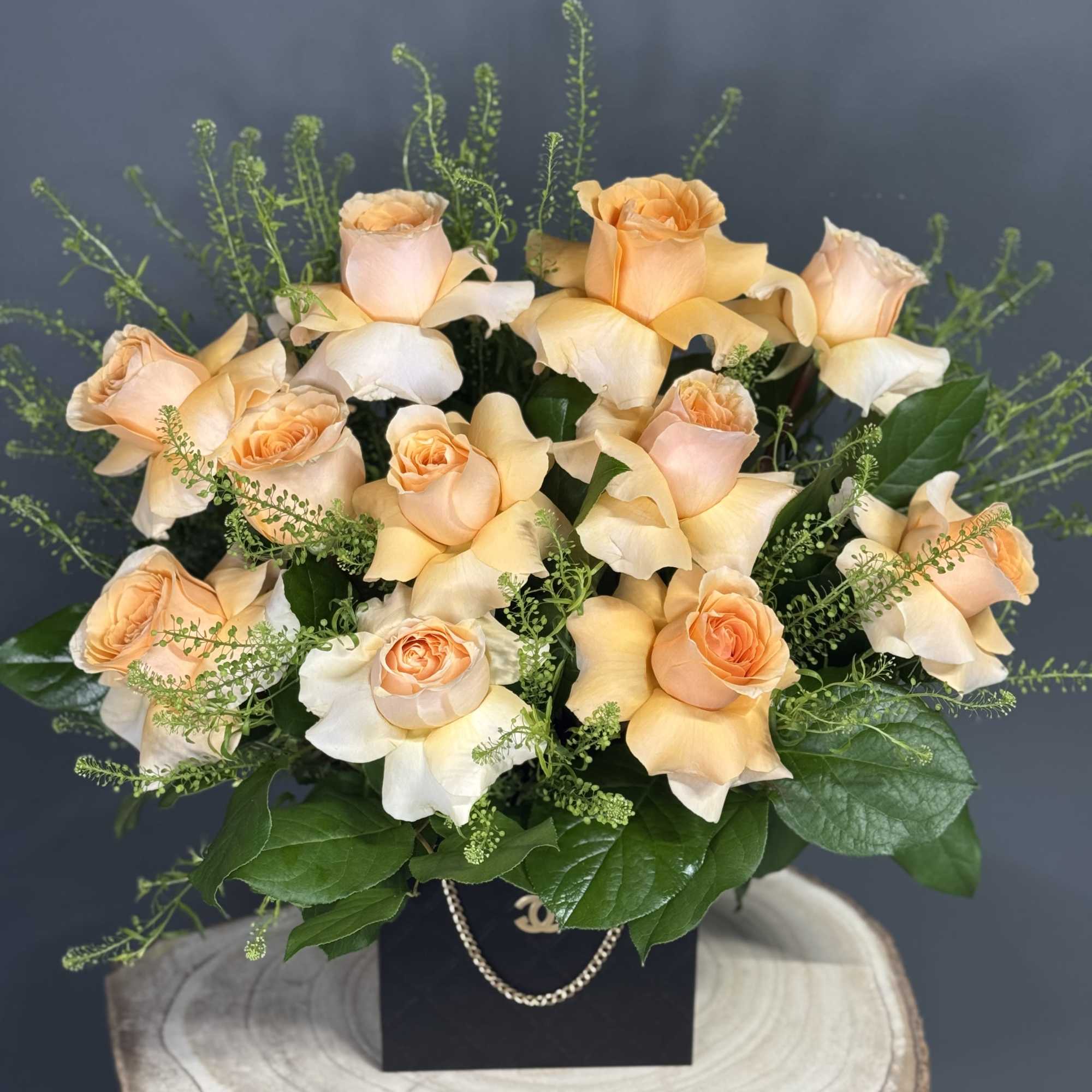 Peach roses arranged in a black box with greenery