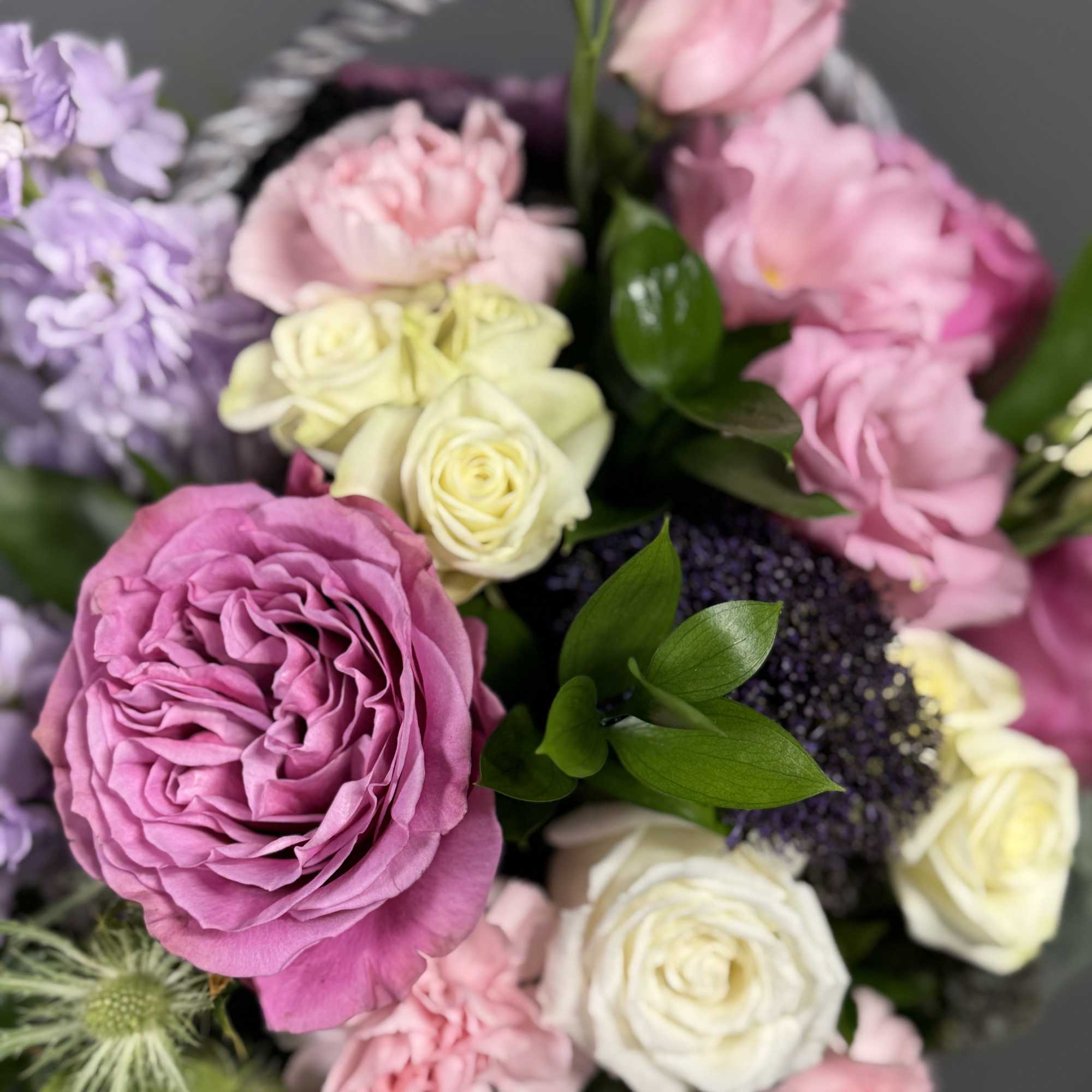 Basket arrangement of pink garden roses, white roses, and pastel flowers in soft spring colors